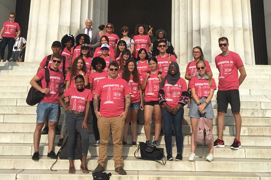 Group of diverse young people wearing matching red Washington DC T-shirts posing on marble steps outdoors.