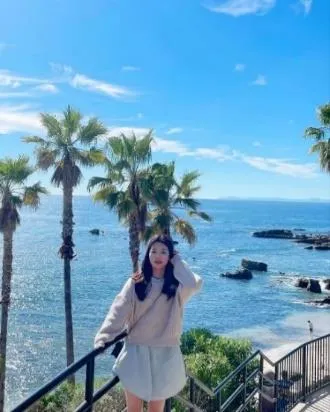 Woman standing on stairs by ocean with palm trees under a blue sky.