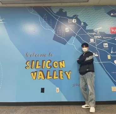 Young professional intern with arms crossed in front of Silicon Valley map wall mural.