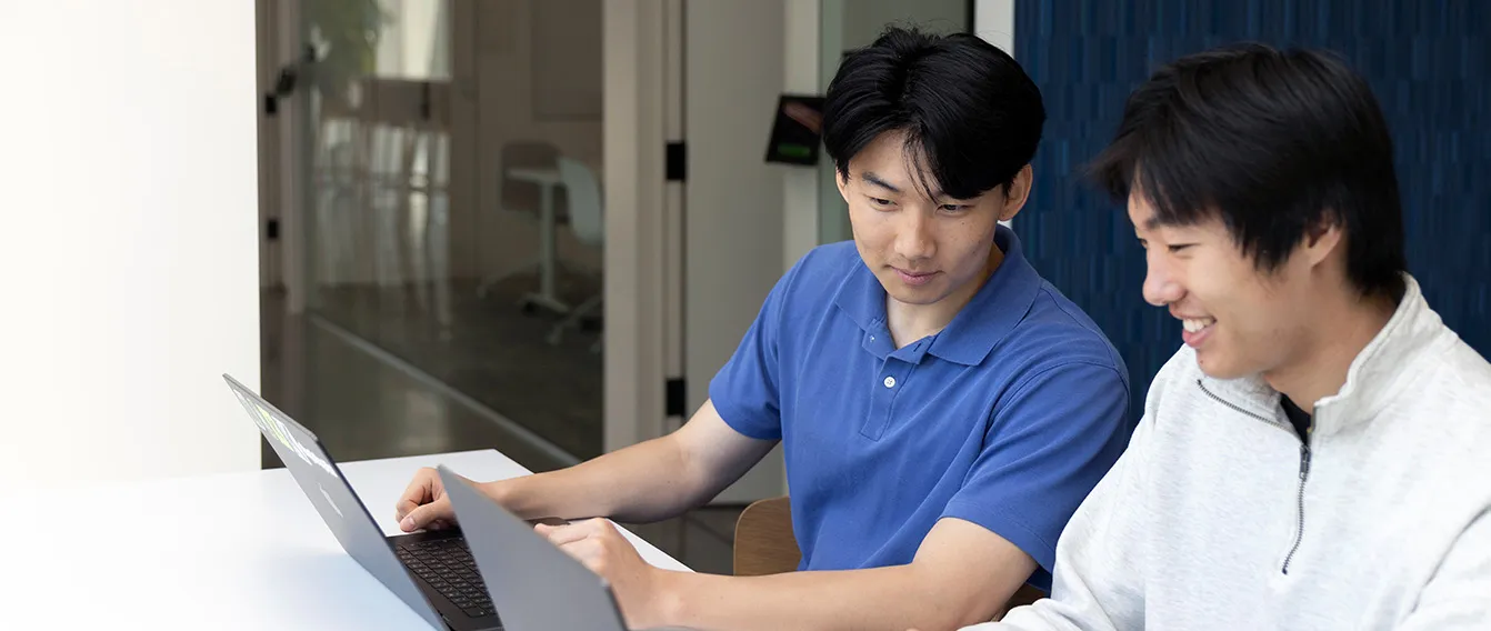 Two diverse young professionals collaborating at a desk with laptops and documents in an office.