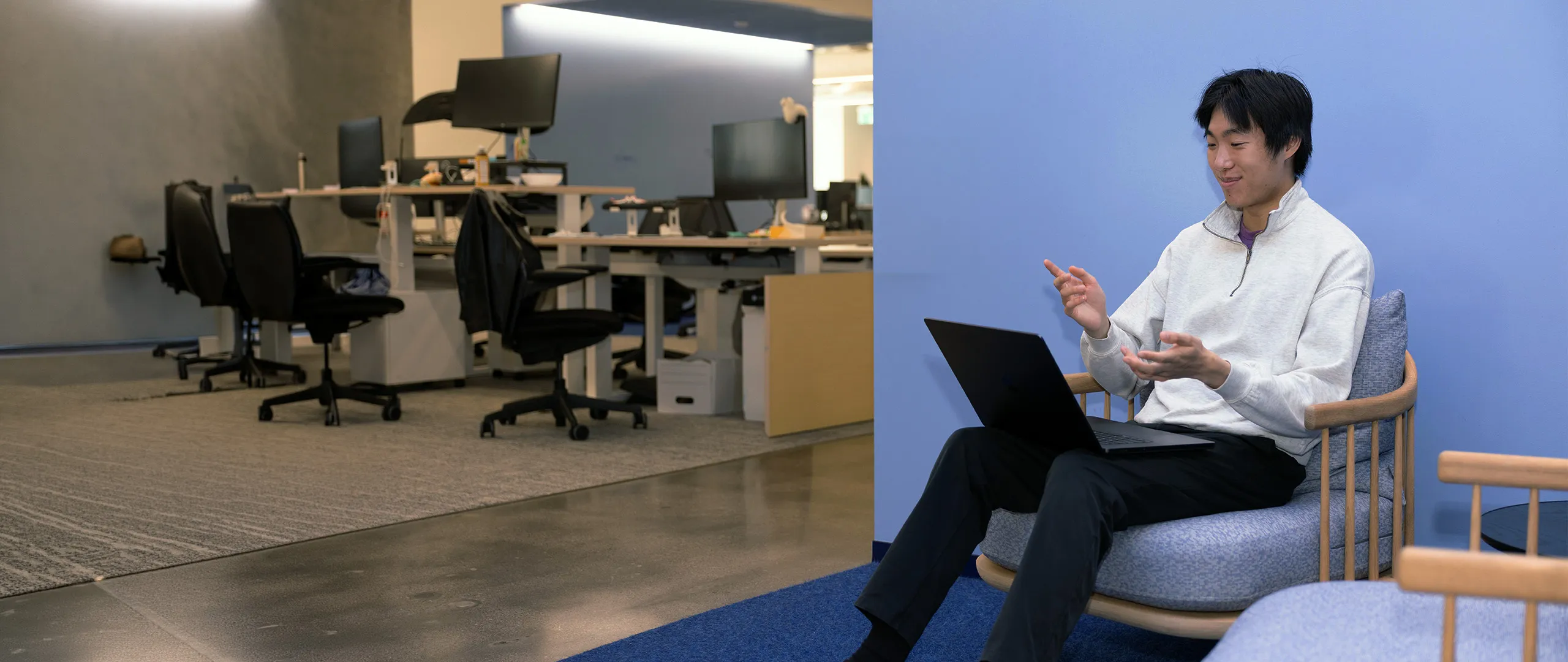 Man and woman using laptops separately in a blue-walled office room with a bookshelf and table.