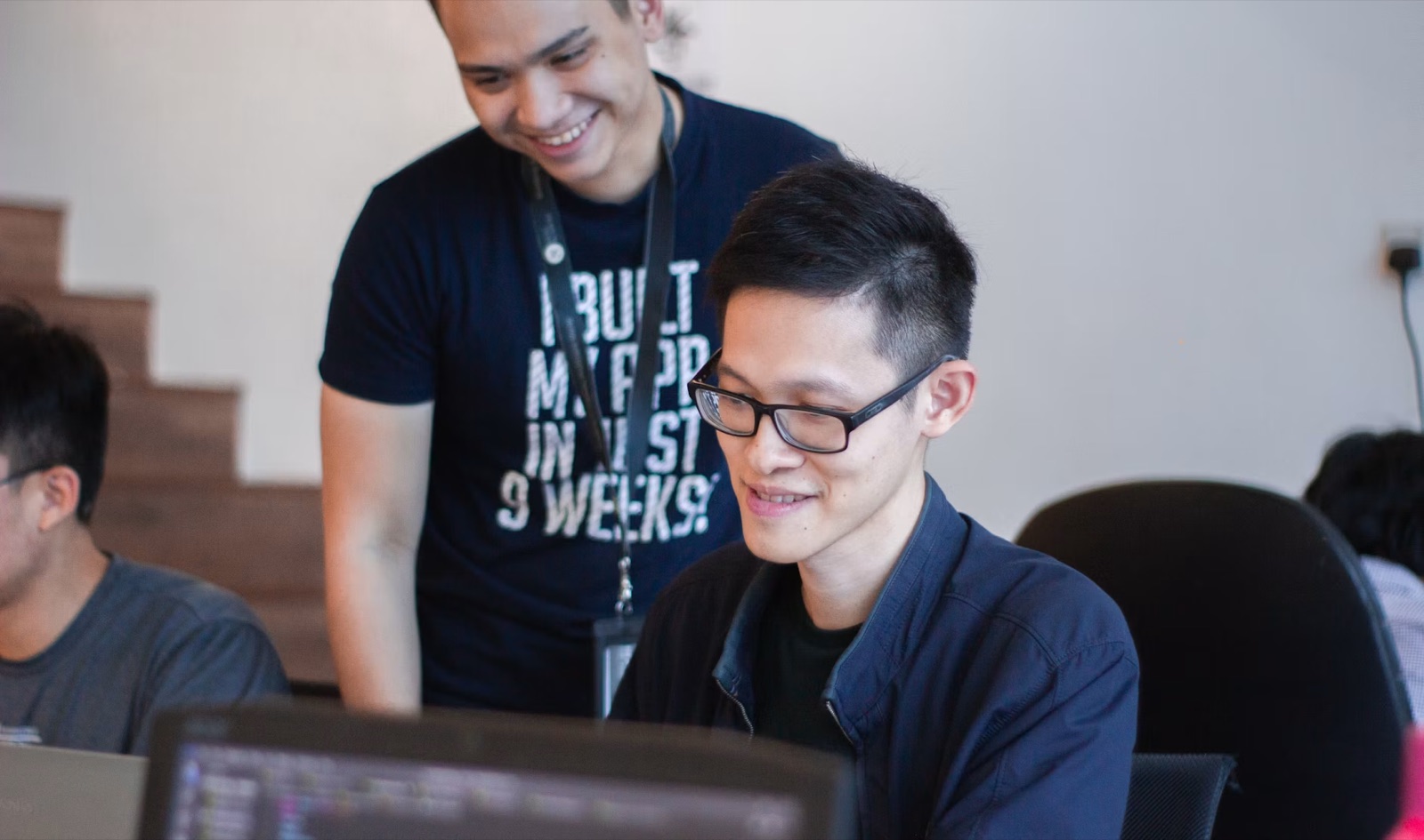 Smiling mentor looking over a young professional’s shoulder as they work on a laptop