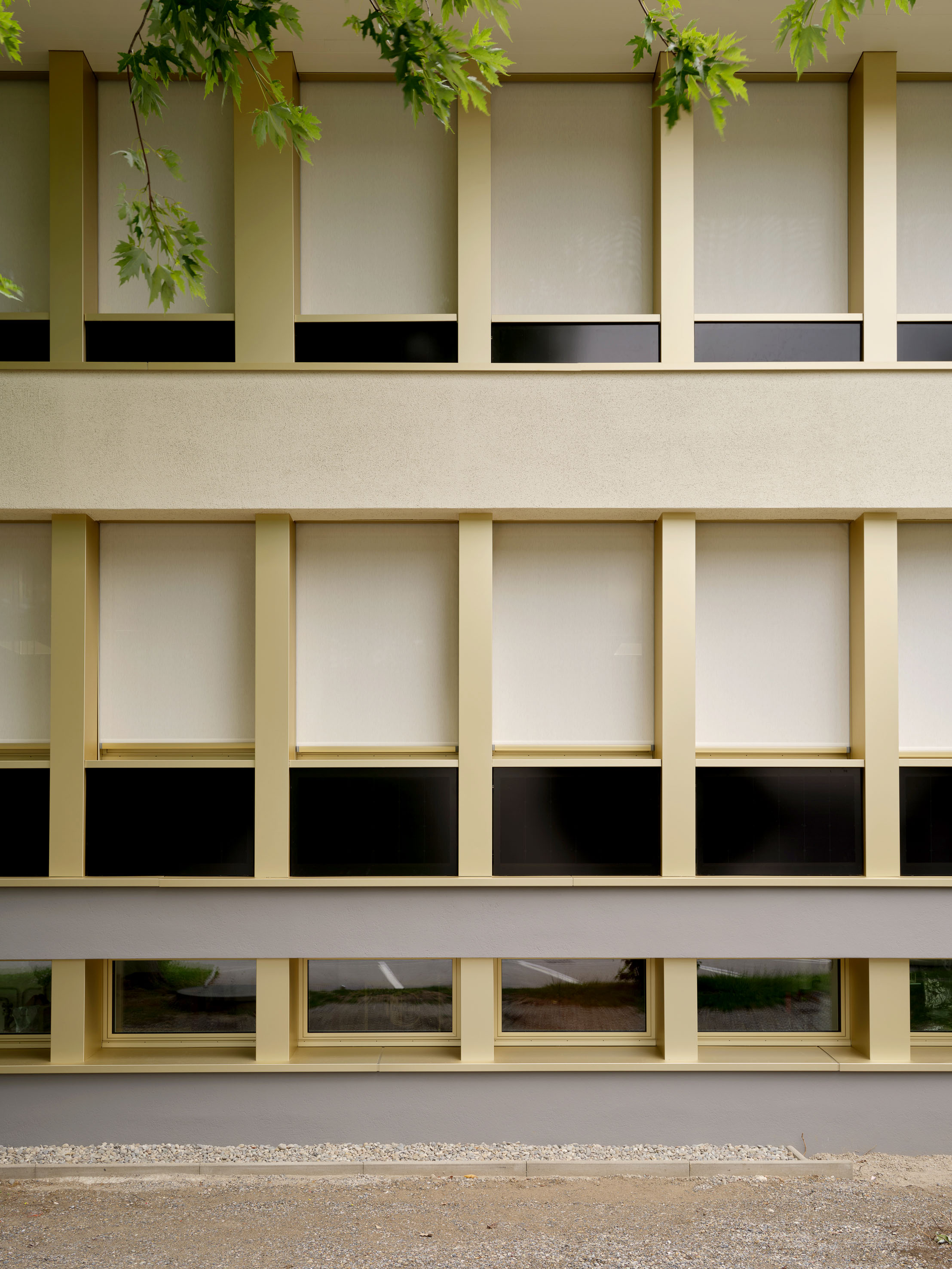 Fassadendetail des Gemeindehauses Turbenthal mit hellen Profilen, Sonnenschutz und dunklen Photovoltaikpaneelen.