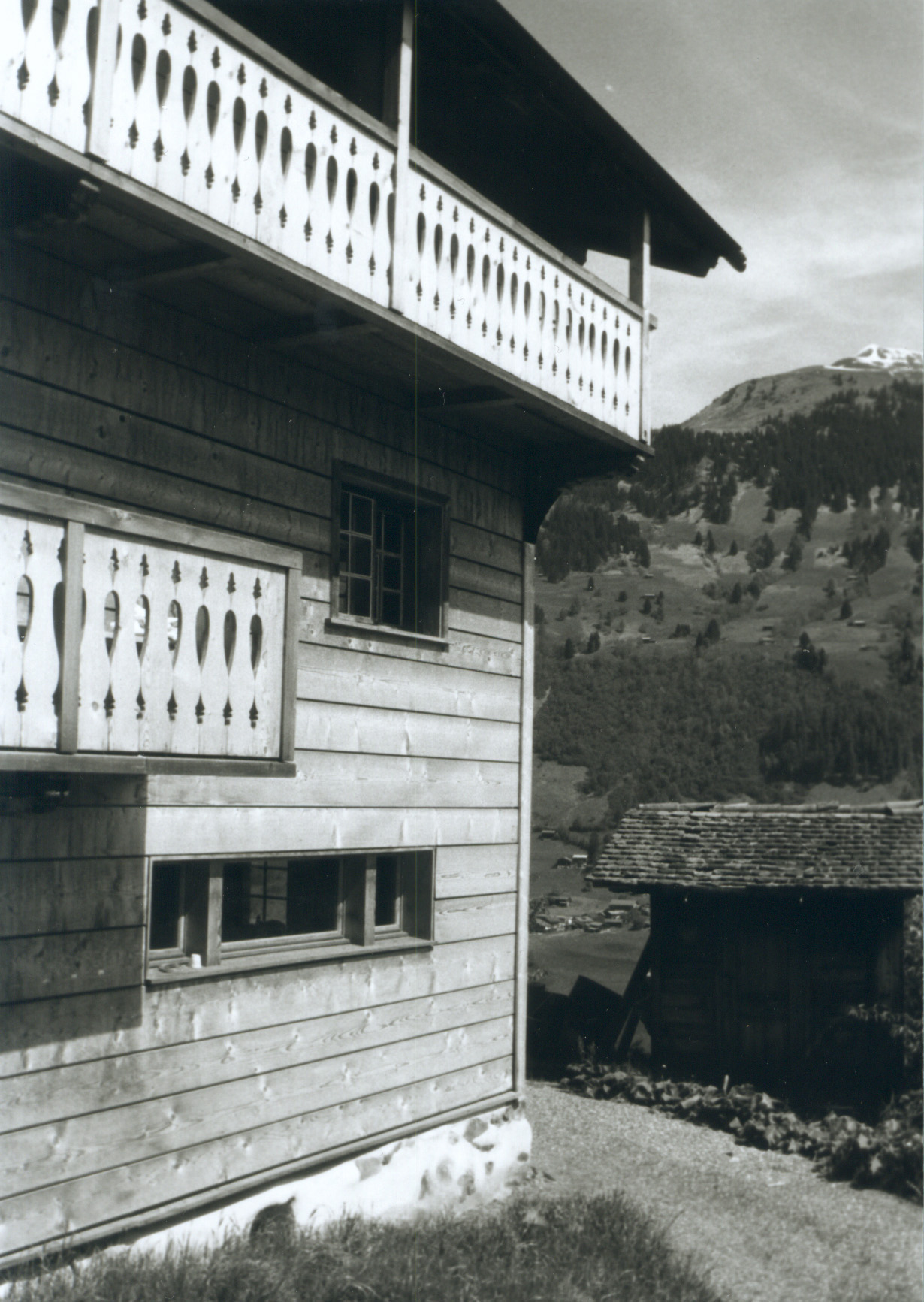 Holzfassade und Lauben von Haus Conters vor einem bewaldeten Berghang.