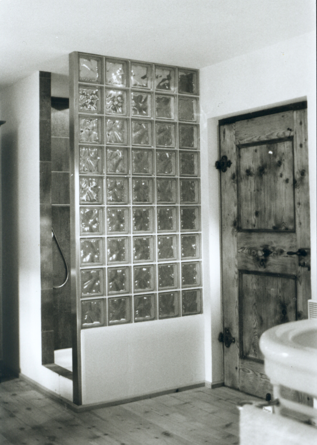 Dusche in Haus Conters mit Glasbausteinwand neben einer alten Holztür.