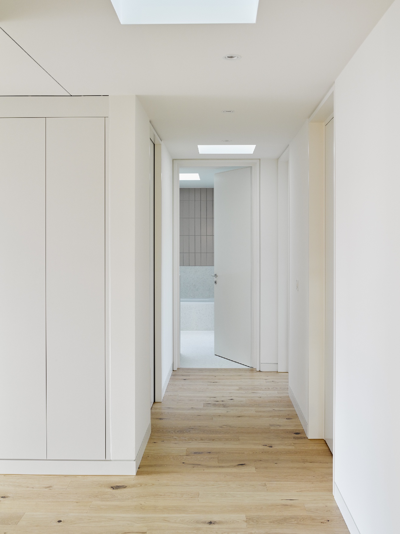 Heller Wohnungskorridor mit Holzboden, weissen Einbauschränken und Oberlichtern.