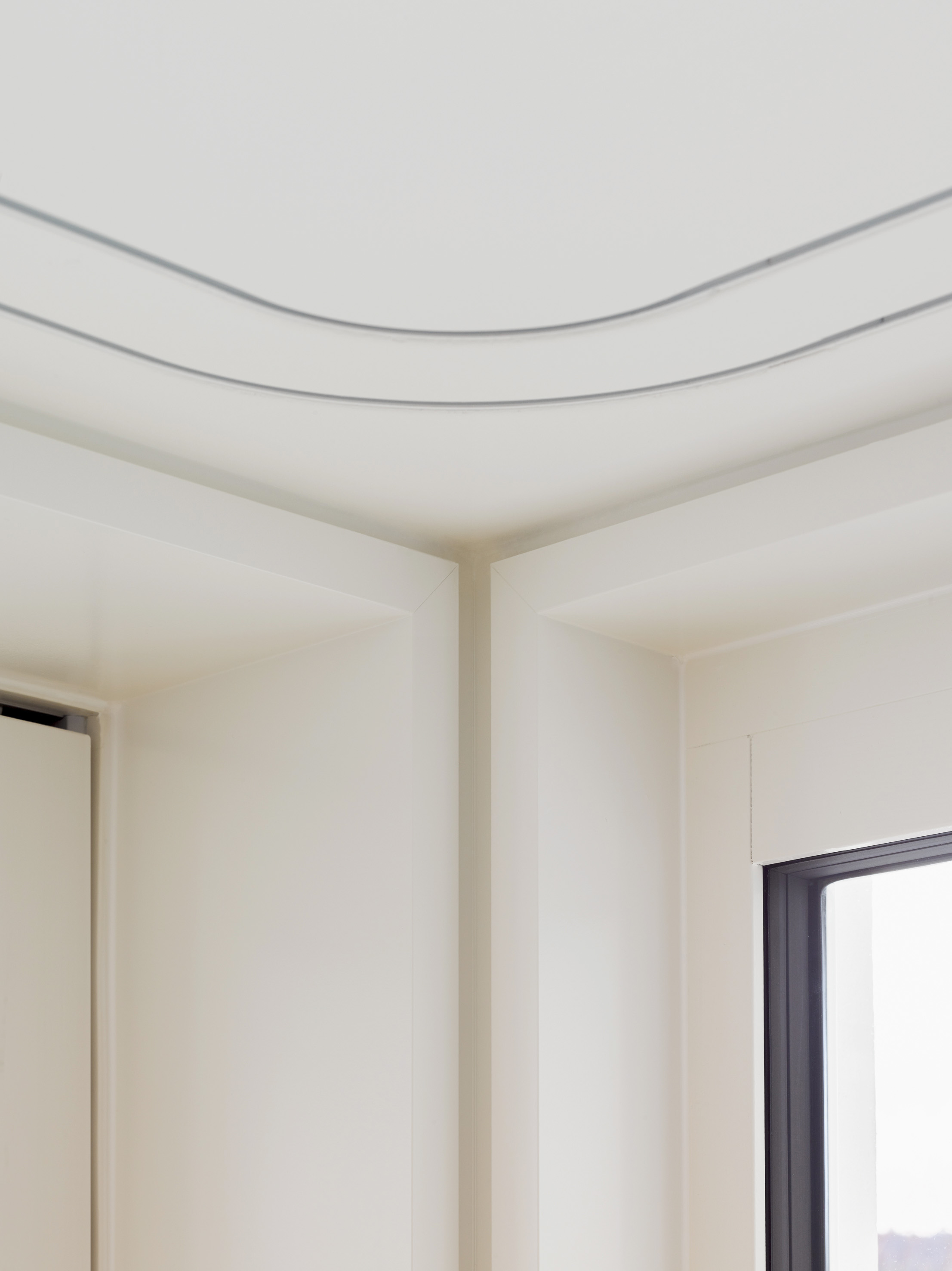 Detail des Fensteranschlusses mit weissen Laibungen und gerundeten Vorhangschienen in der Decke.
