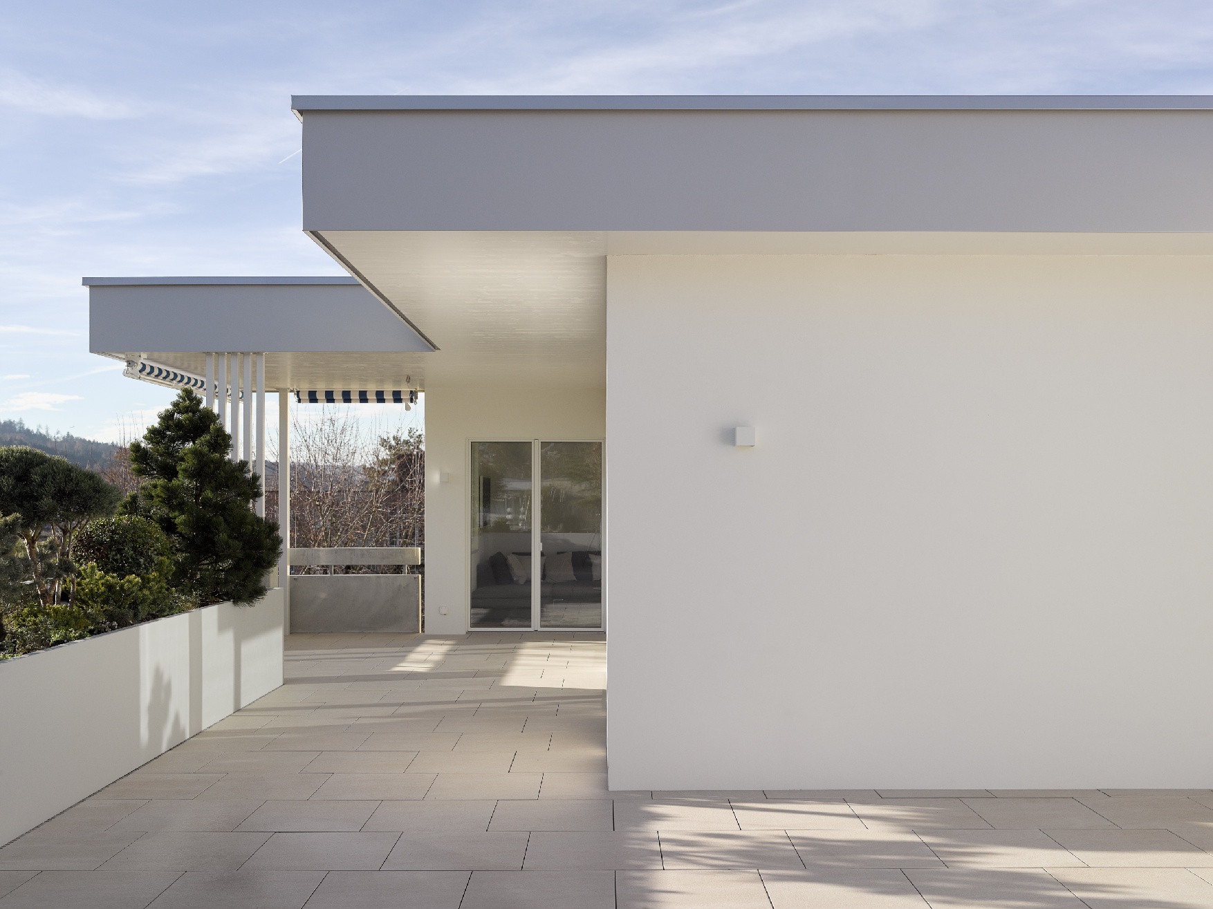 Dachterrasse mit hellen Bodenplatten, bepflanzter Brüstung und weit auskragendem Dach.