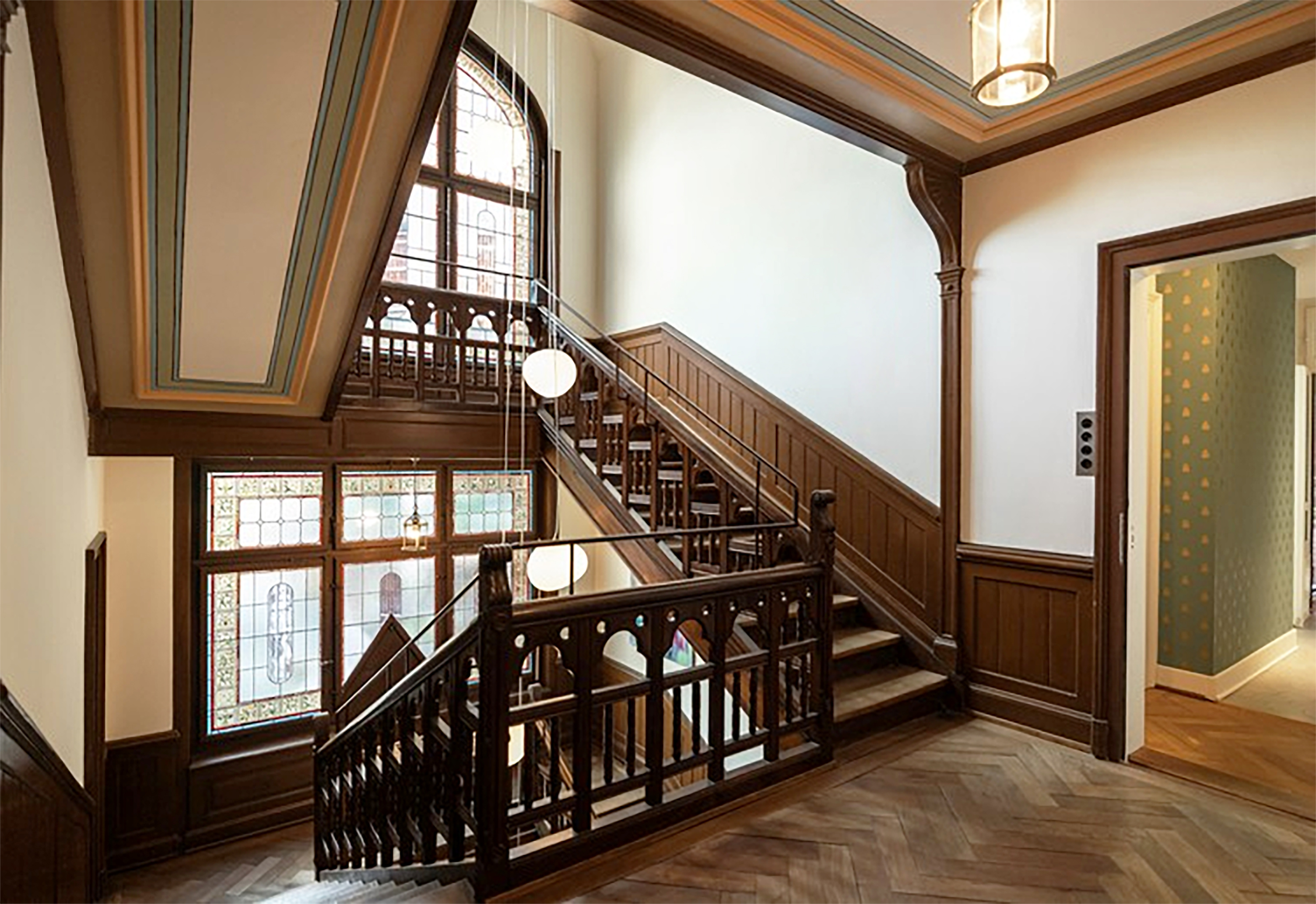 Restauriertes Treppenhaus der Villa Lindeneck mit Holzgeländern, farbig gefasster Decke und historischen Bleiverglasungen.