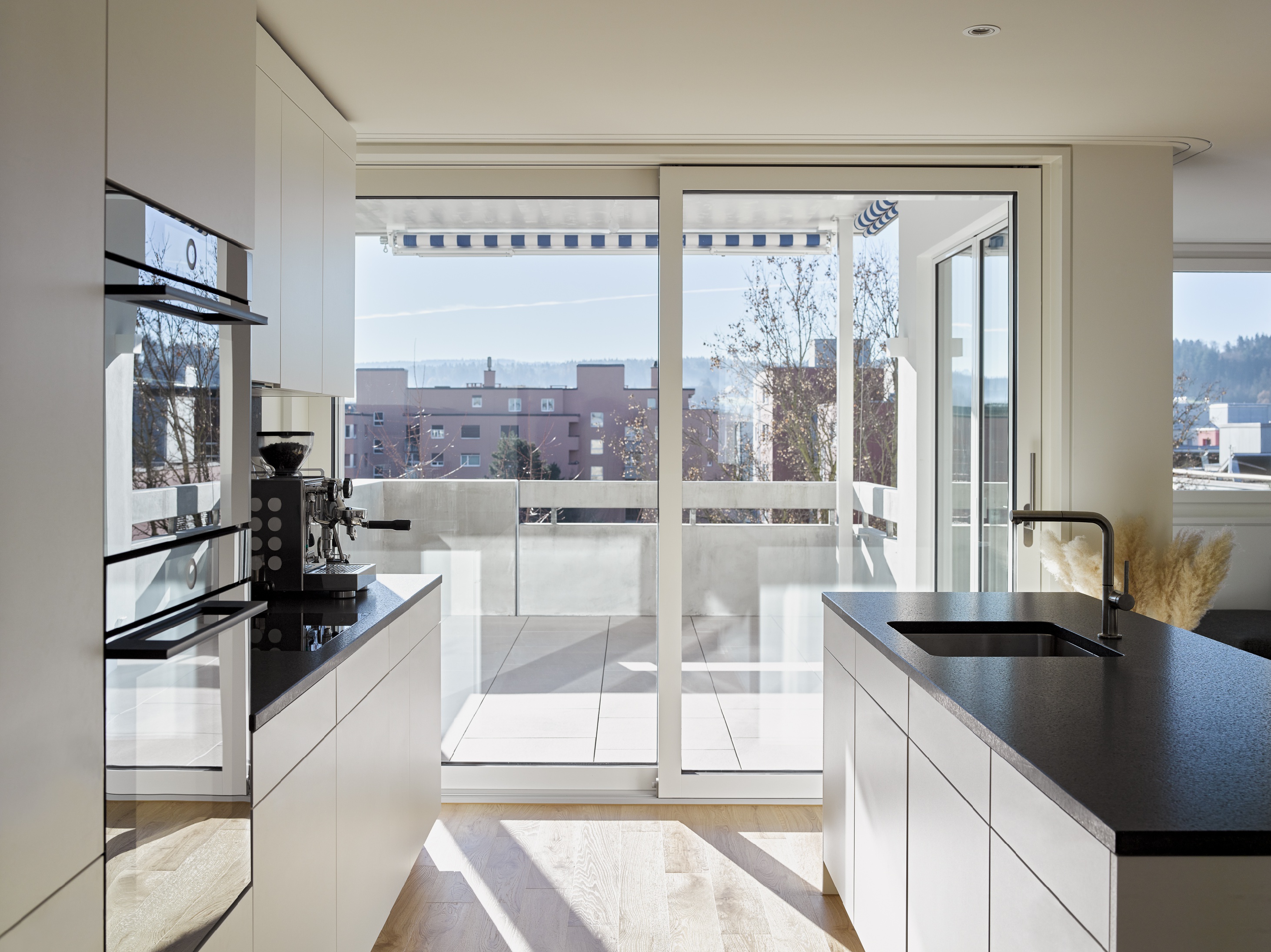 Blick zwischen Küchenzeile und Insel durch eine bodentiefe Glasfront auf die Dachterrasse.