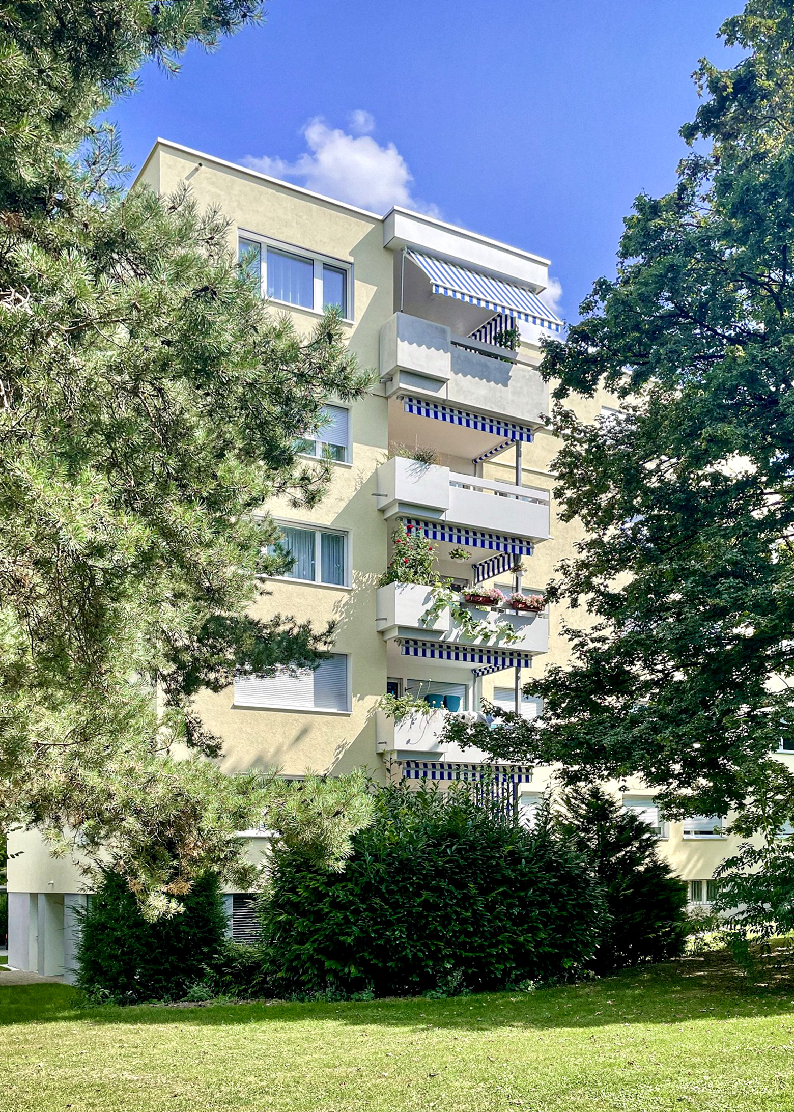 Hofansicht des sanierten Mehrfamilienhauses Wingertlistrasse 16/18 mit Balkonen, gestreiften Markisen und altem Baumbestand.