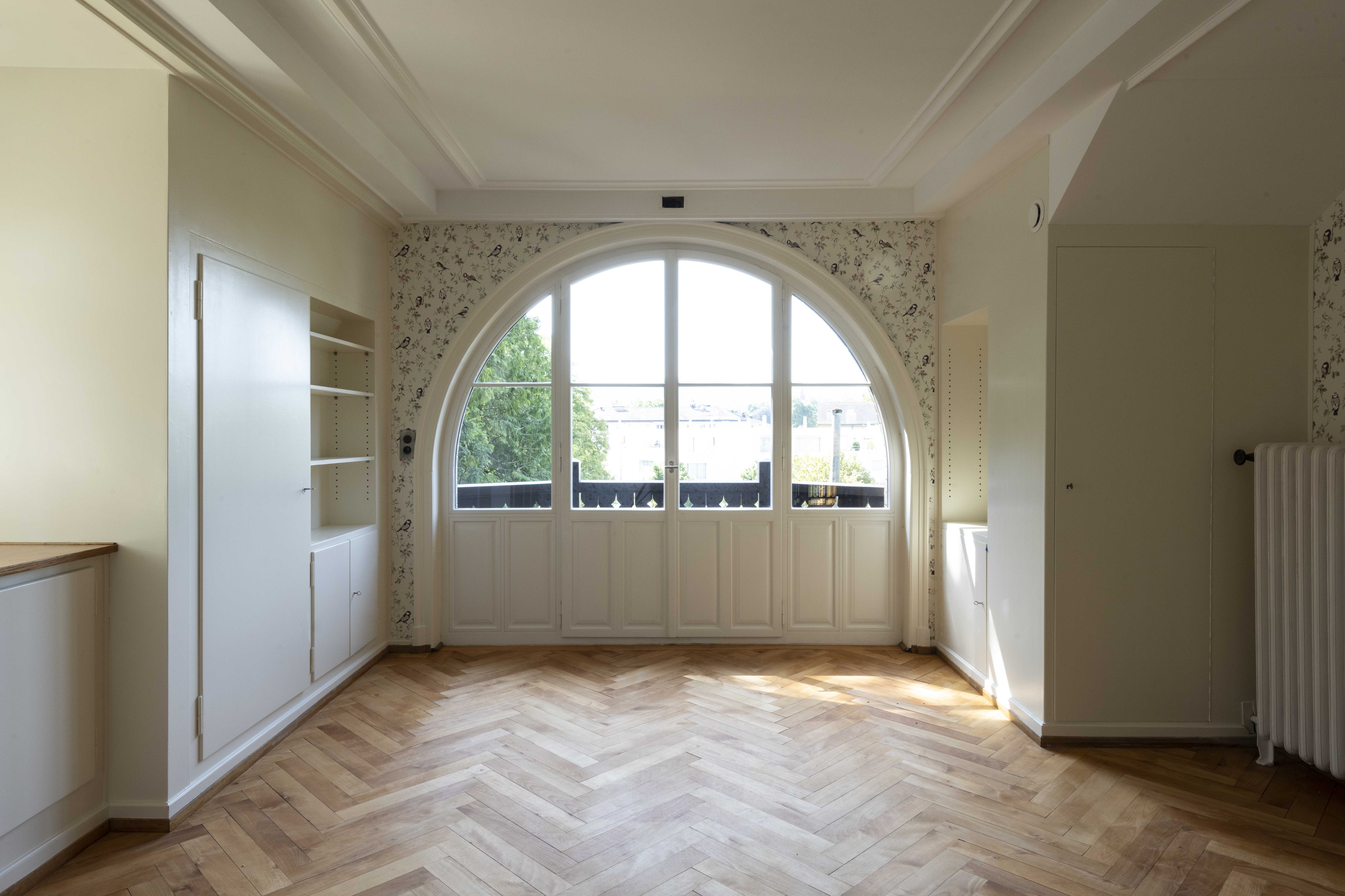Rapunzelzimmer im Geburtshaus Winterthur mit grossem Bogenfenster, Fischgrätparkett und hellen Einbauschränken.