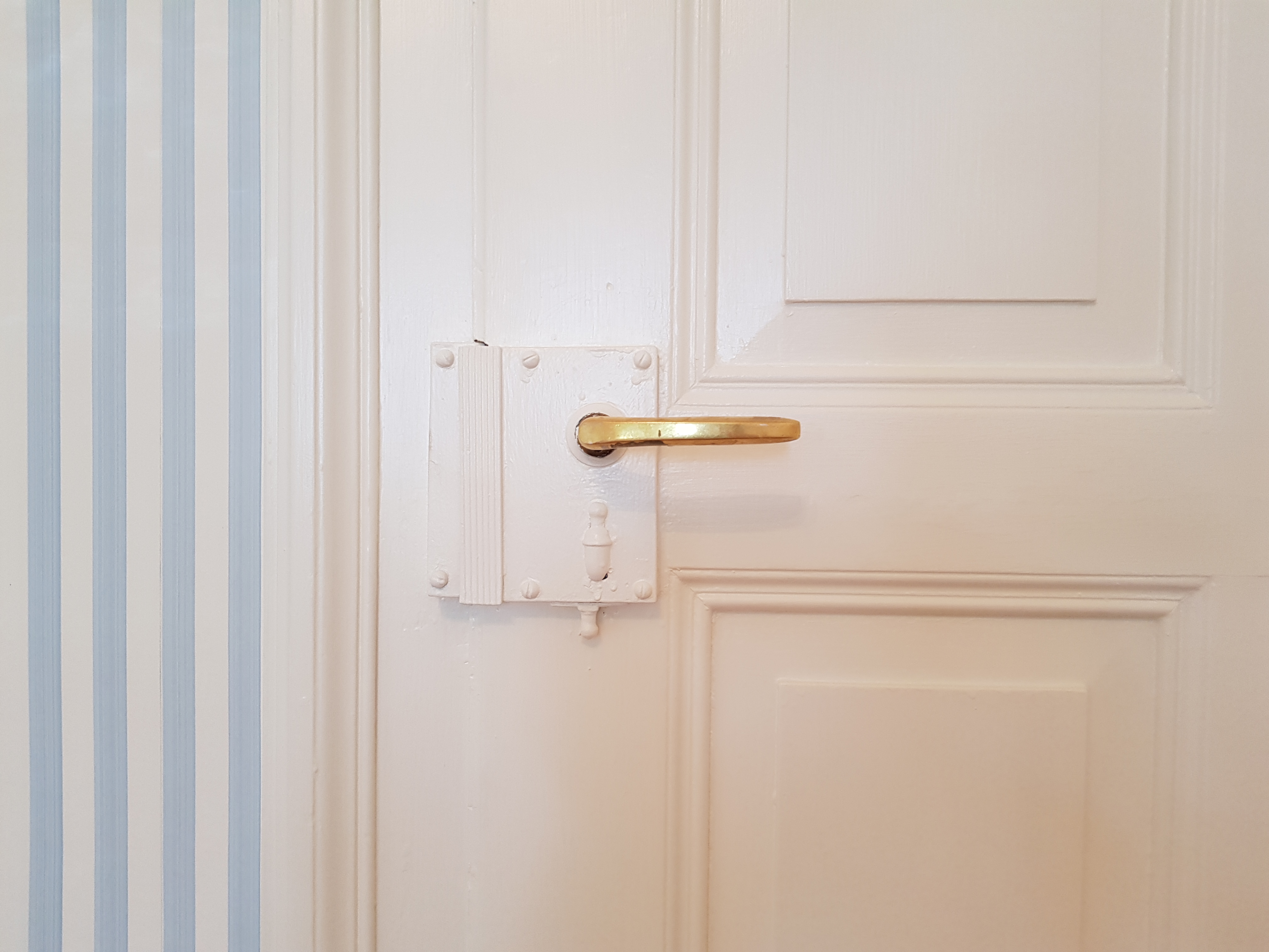 Weiss gestrichene Kassettentür mit Messinggriff neben blau-weisser Streifentapete in der Villa Lindeneck.