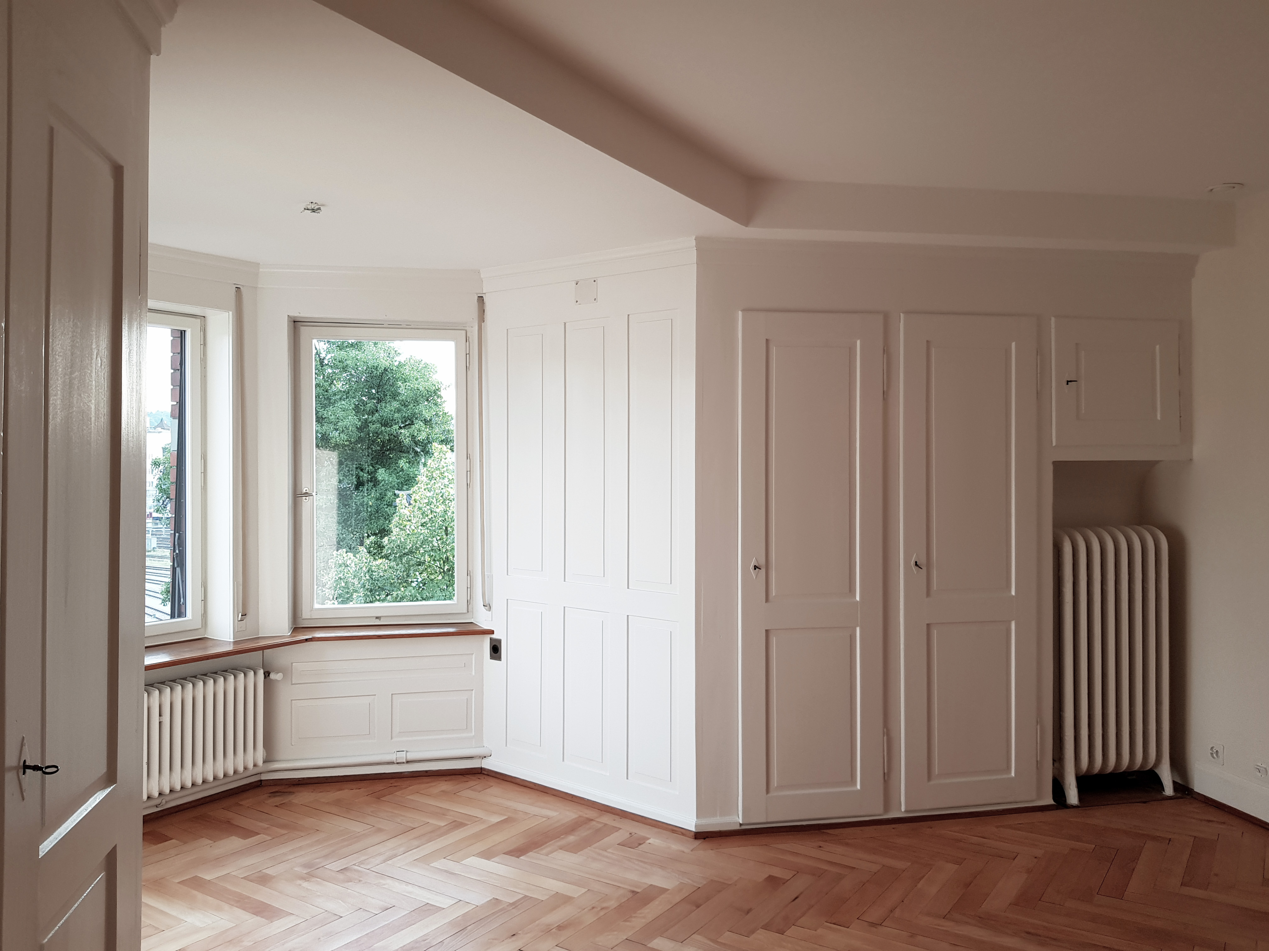 Turmzimmer der Villa Lindeneck mit Erkerfenstern, Fischgrätparkett und weissen Einbauschränken.