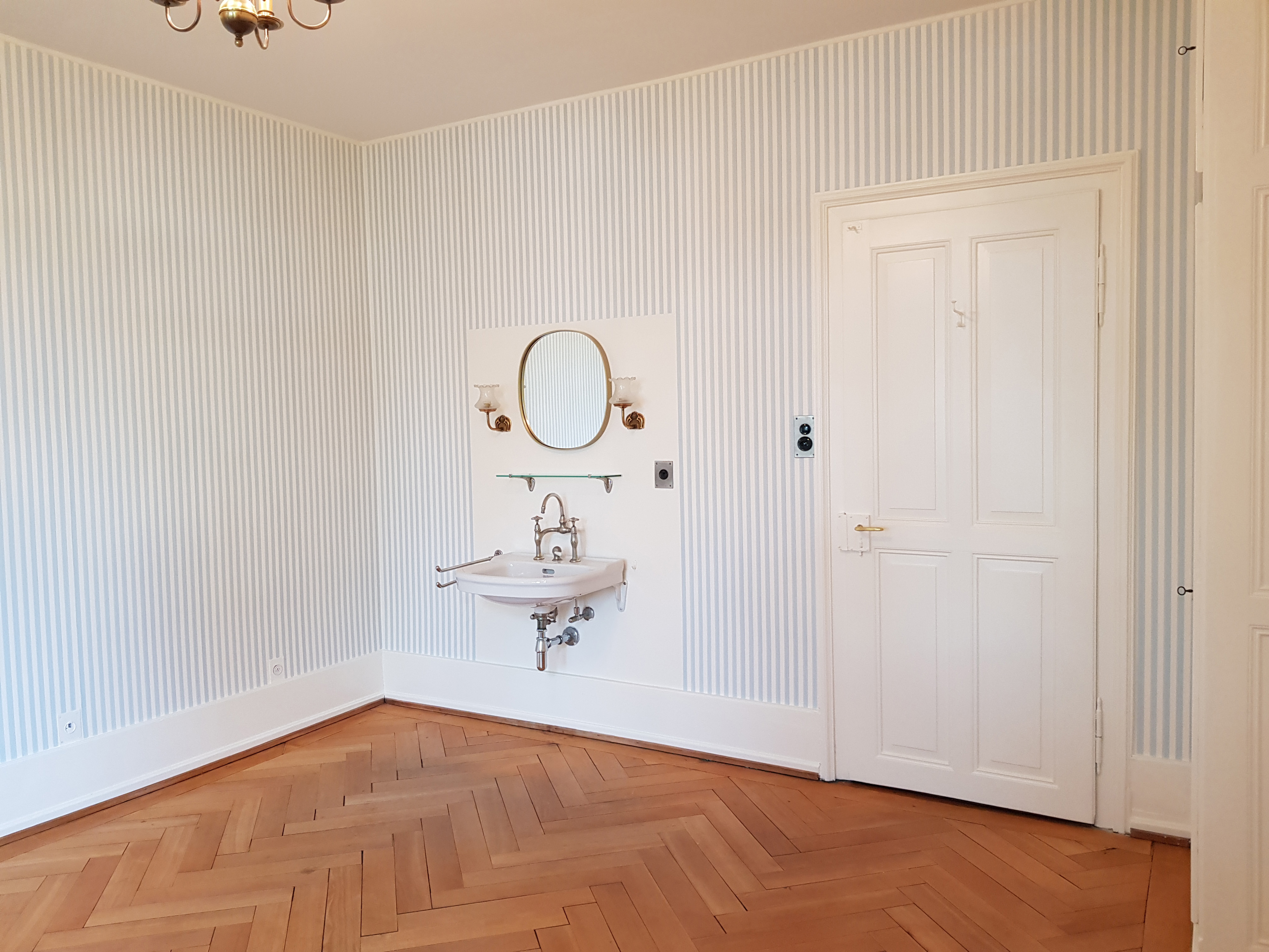 Historischer Raum der Villa Lindeneck mit Streifentapete, Fischgrätparkett und Waschtisch mit Spiegel.