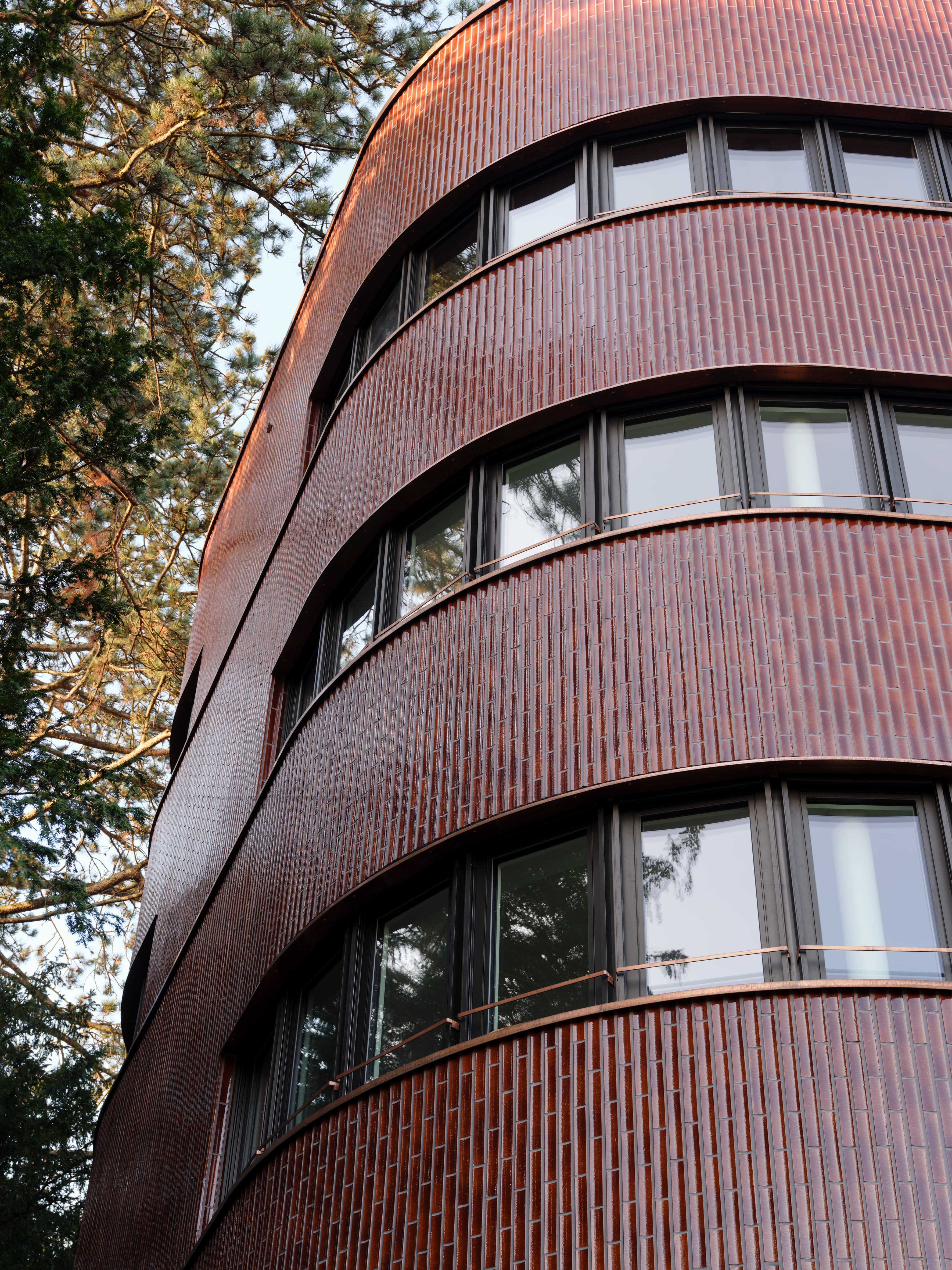 Blick nach oben auf die gerundete Terrakottafassade des Ergänzungsbaus Lindeneck mit durchlaufenden Fensterbändern.