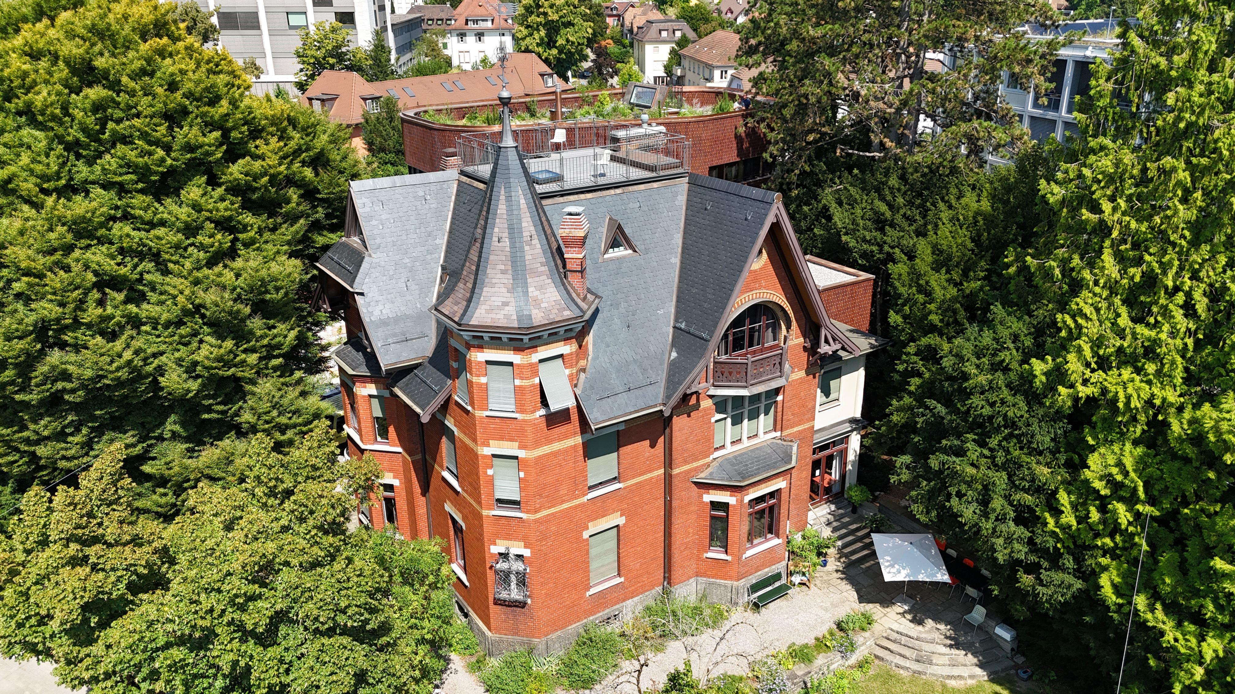 Luftaufnahme der Villa Lindeneck mit Turm, Schieferdach und umgebendem Baumbestand.