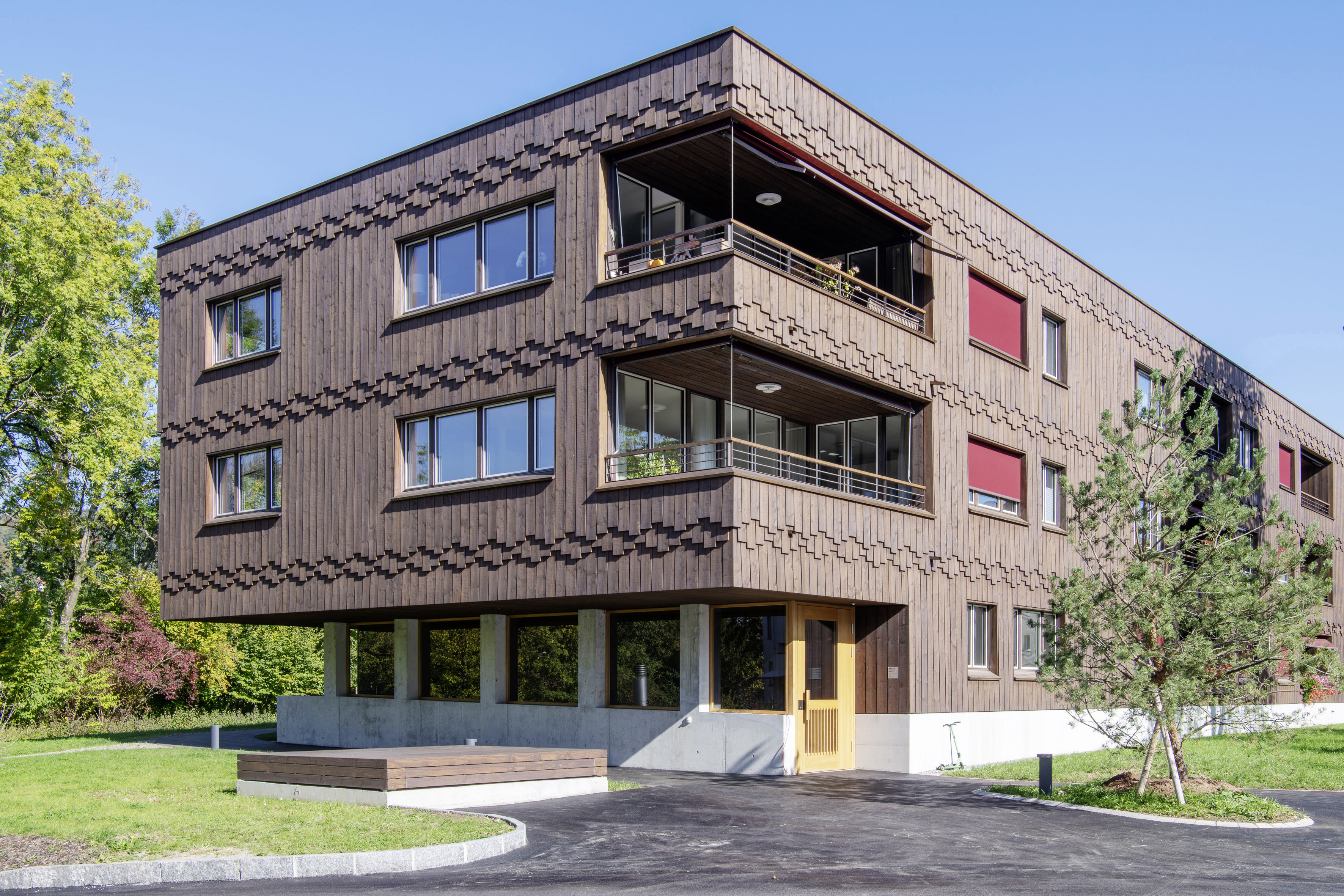 Hauptgebäude der Wohnanlage Grünmatt mit Holzfassade, Eckbalkonen und Café im Erdgeschoss.