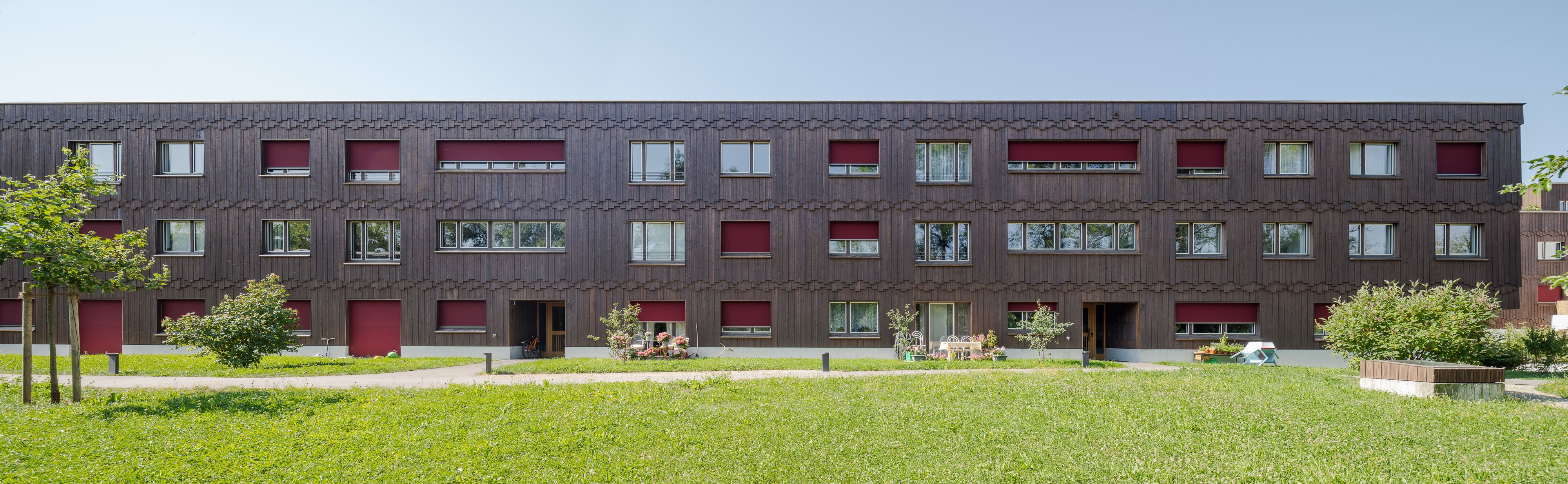 Nordfassade von Haus A der Wohnanlage Grünmatt mit rotem Sonnenschutz und vorgelagerter Wiese.
