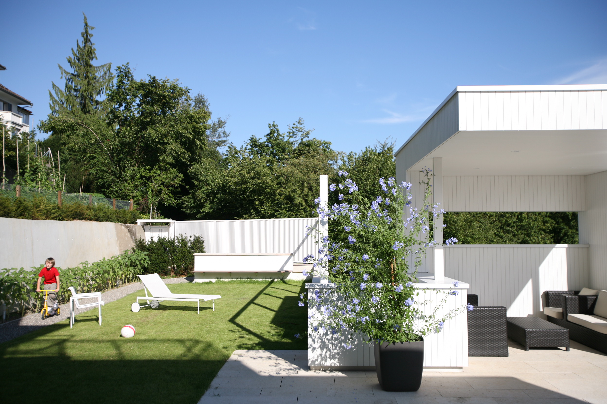 Ostgarten von Haus Trottenweg mit Rasenfläche, Liegestuhl und überdachtem Sitzplatz.