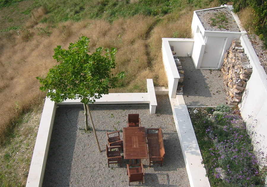 Terrassierter Gartensitzplatz mit Kiesboden, Holztisch und weissen Stützmauern.