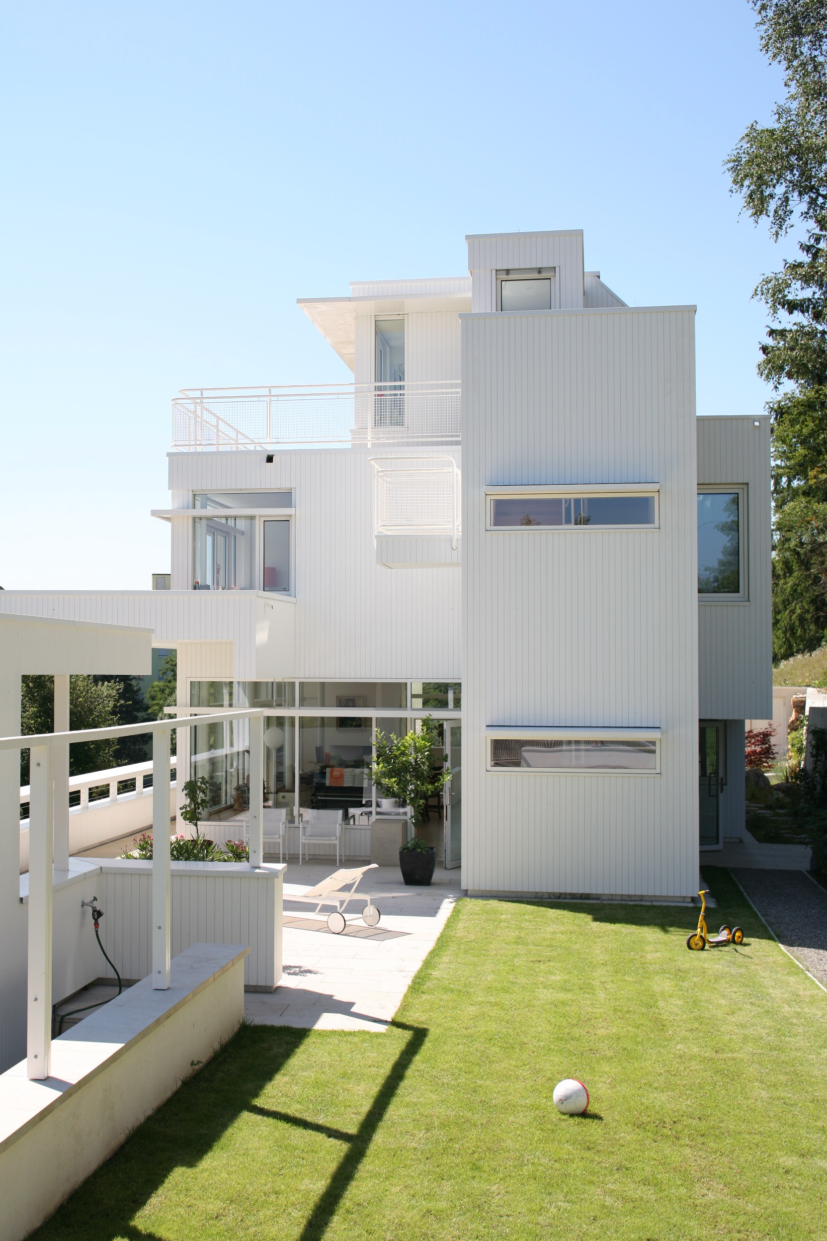 Ostansicht von Haus Trottenweg mit weisser Fassade, Terrasse und vorgelagertem Rasen.