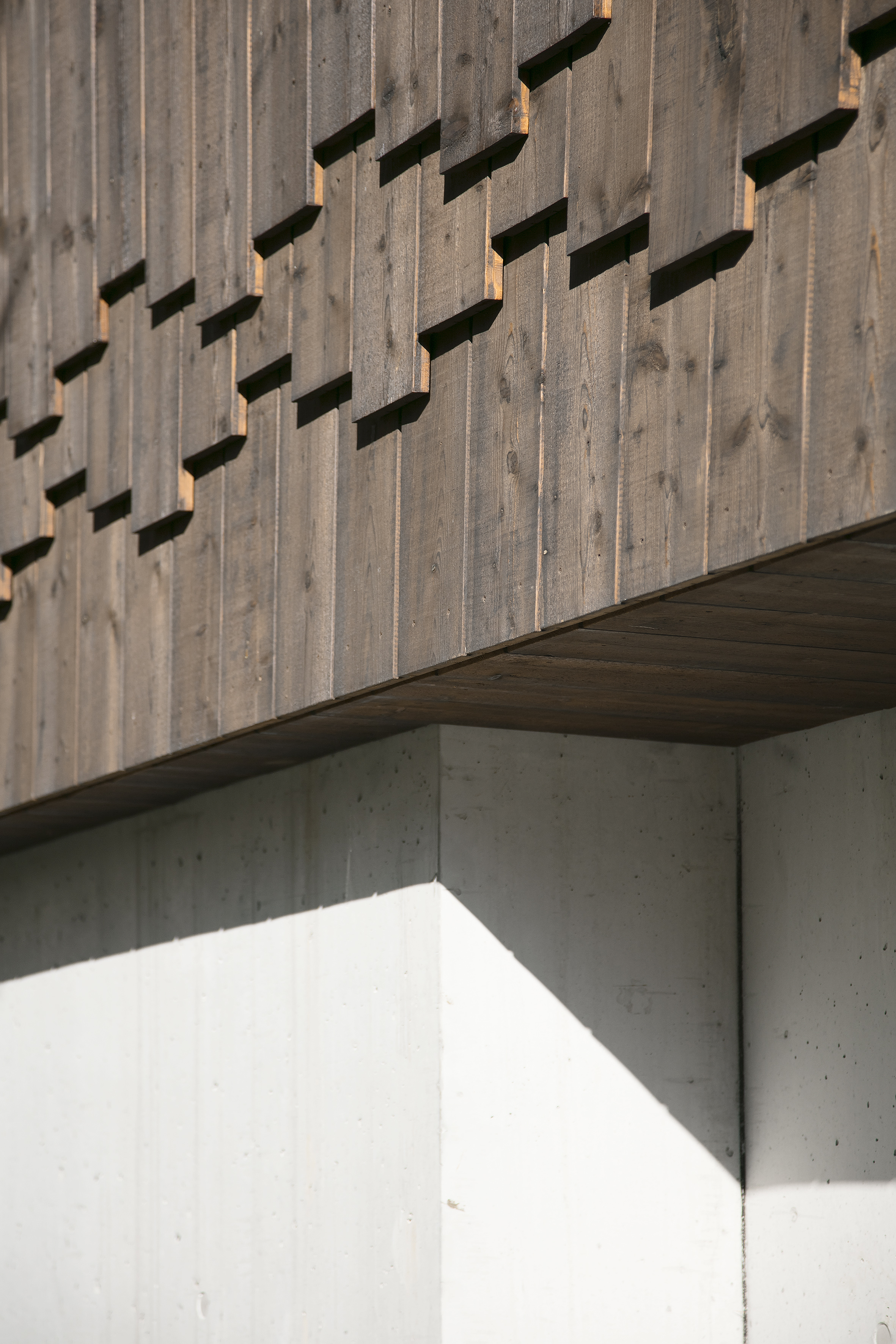 Fassadendetail der Wohnanlage Grünmatt mit überlappenden Holzbrettern über einem Betonsockel.