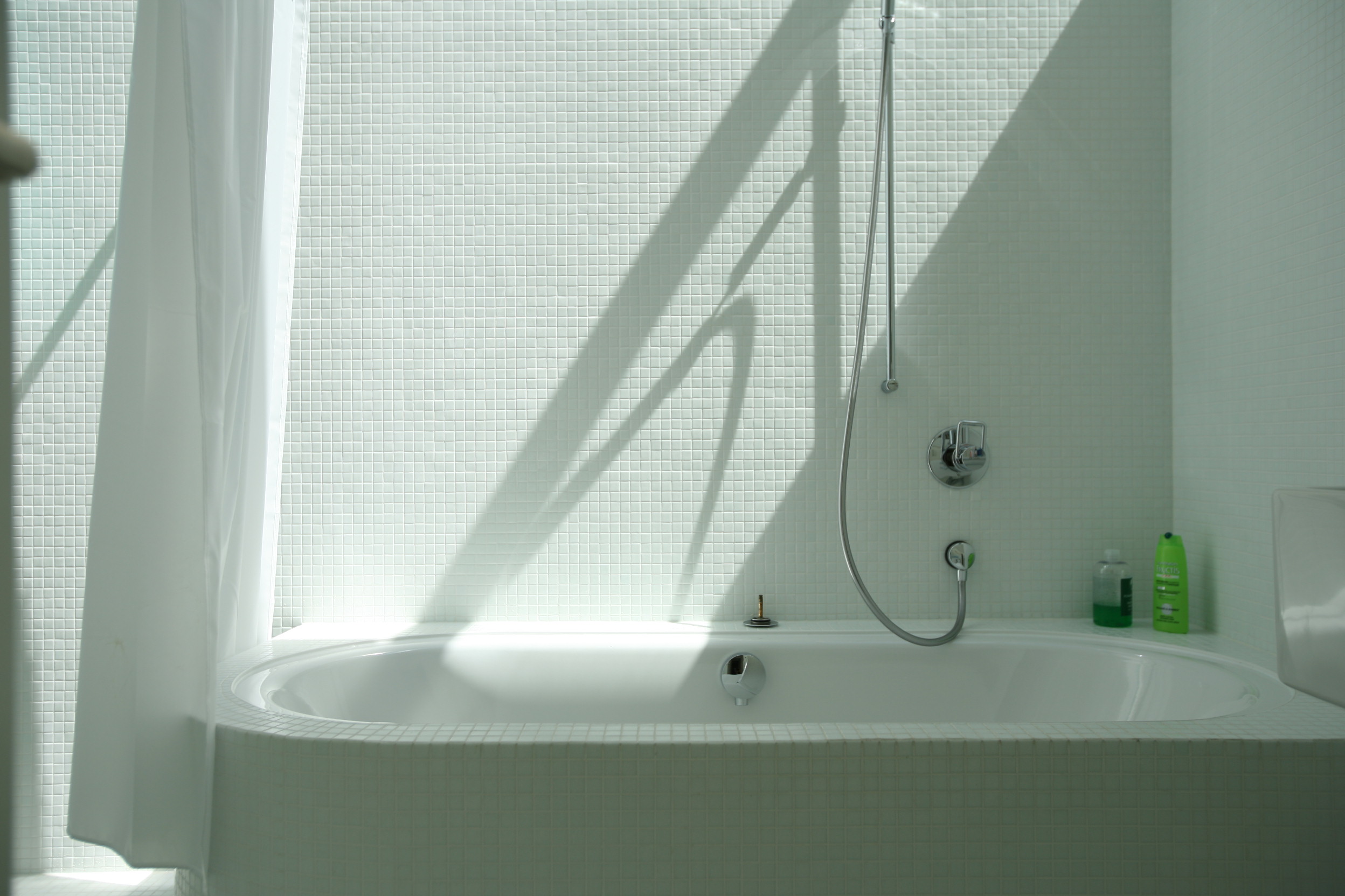 Badewanne im ersten Obergeschoss von Haus Trottenweg mit Mosaikfliesen und einfallendem Sonnenlicht.