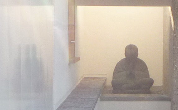Buddhafigur in einer beleuchteten Nische neben einer Holzbank im Empfangsbereich.