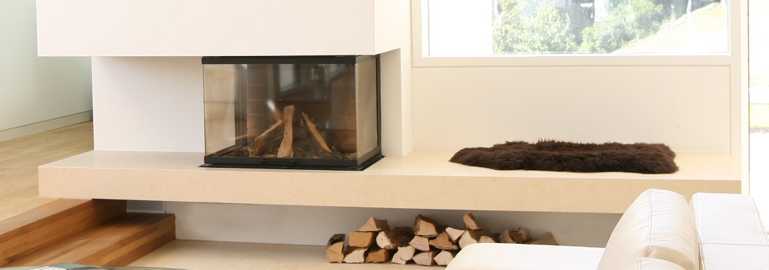 Verglastes Cheminée mit durchgehender Sitzbank und Holzlager im Wohnraum.