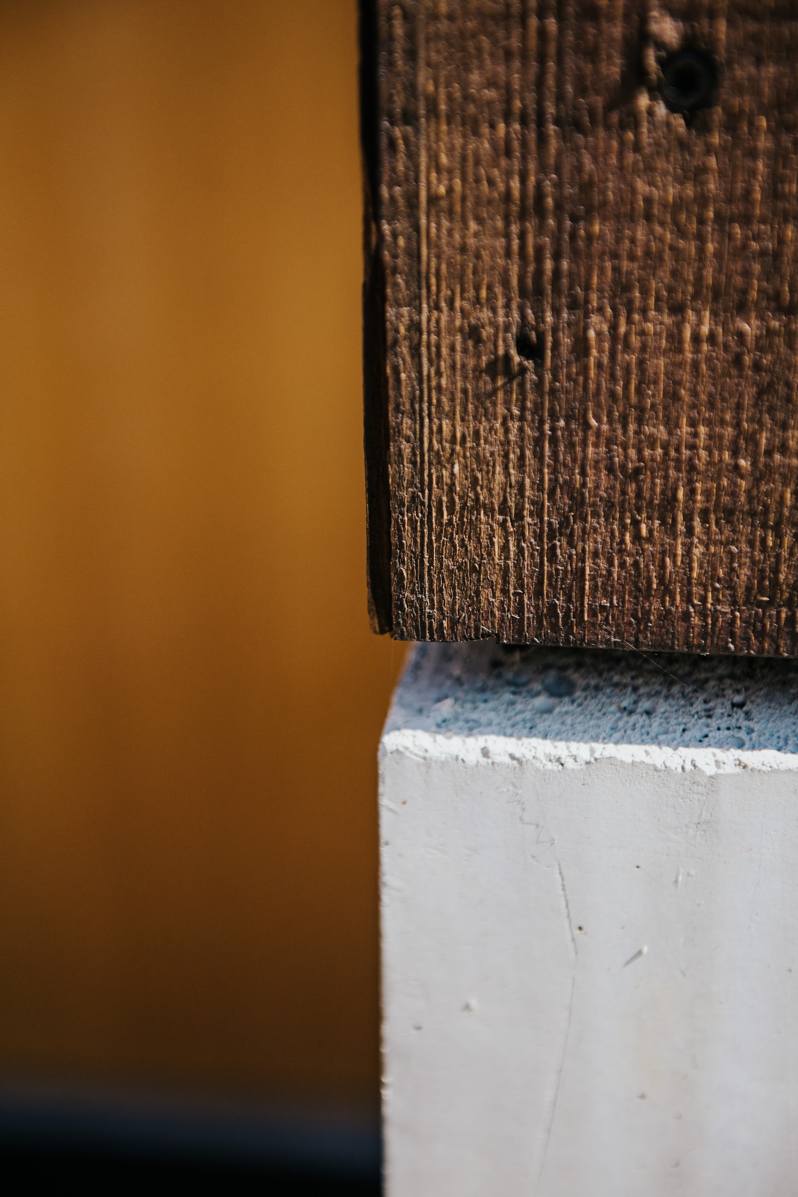 Detail einer rauen Holzfassade über einem hellen Betonsockel.