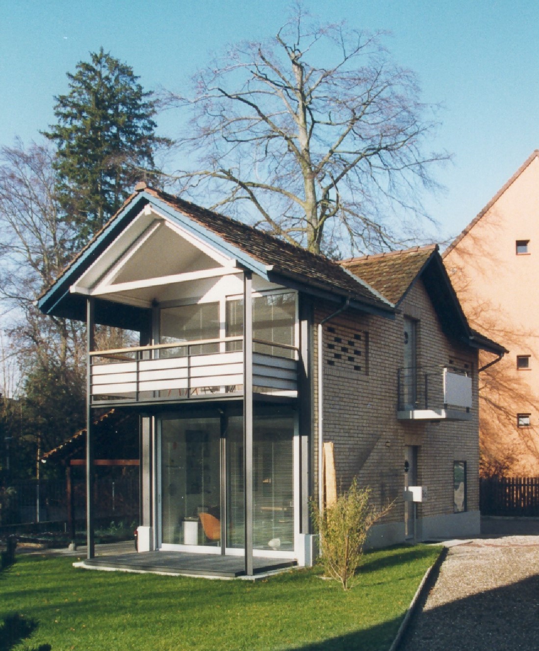Kompaktes Wohnhaus G8 mit Satteldach, verglastem Erdgeschoss und überdachtem Balkon.