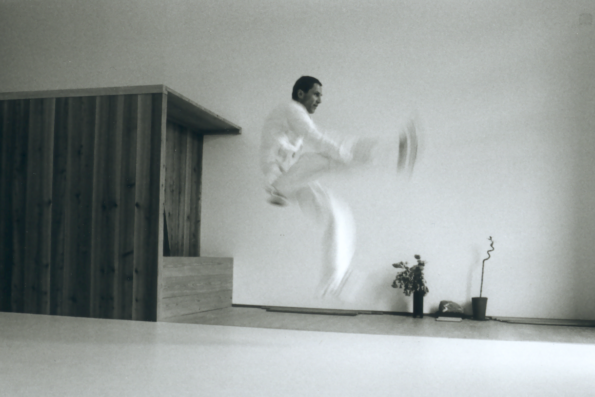 Kampfkünstler beim Sprung im hellen Aikido-Dojo Zürich mit einem hölzernen Raumeinbau.