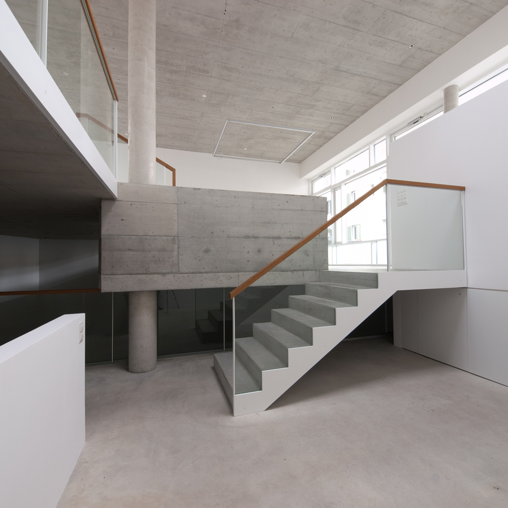 Betontreppe mit Holzhandlauf verbindet die Ebenen der Galerie T77.