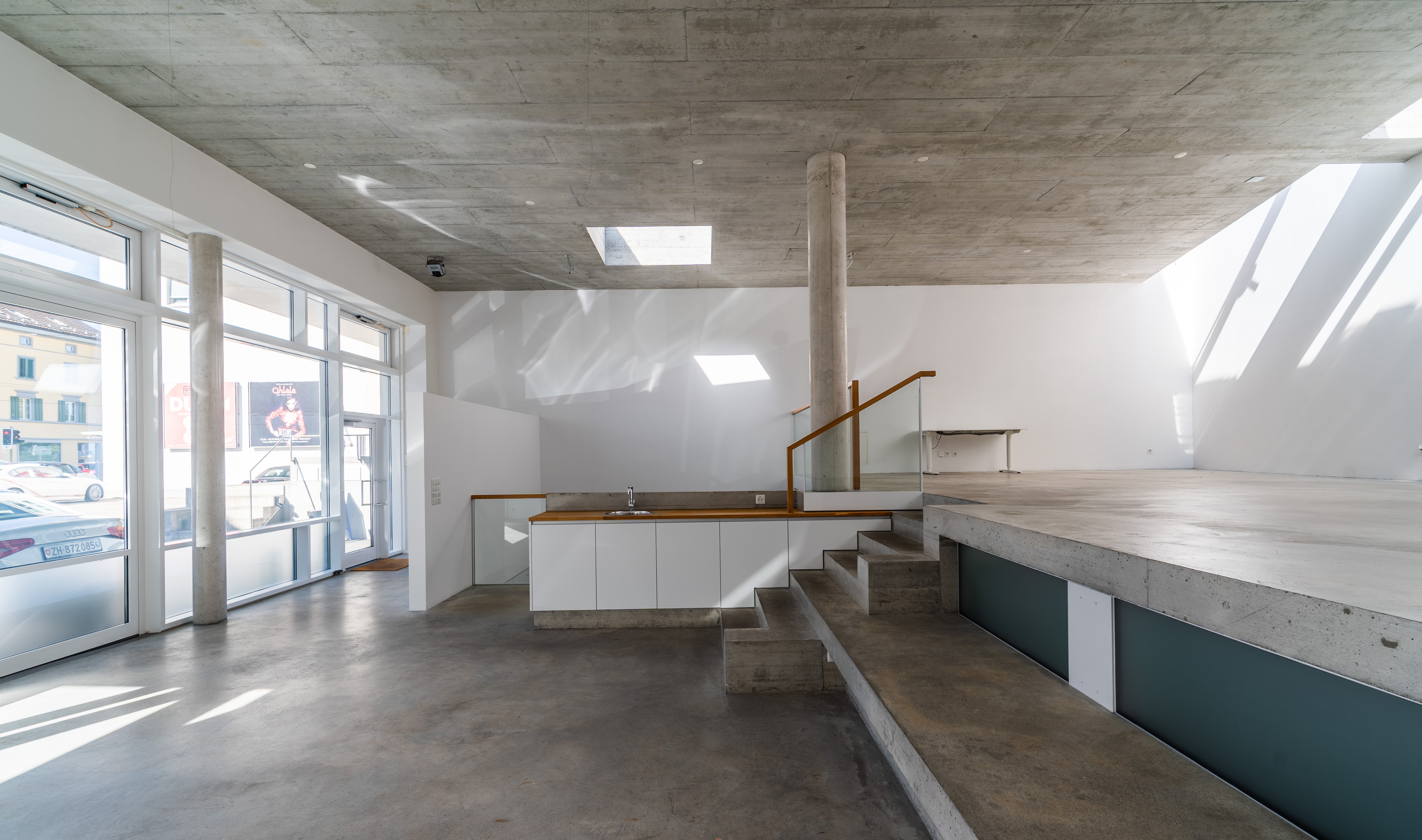 Galerie T77 mit grossen Schaufenstern, Betontreppe und einer erhöhten Ebene mit Einbauten.