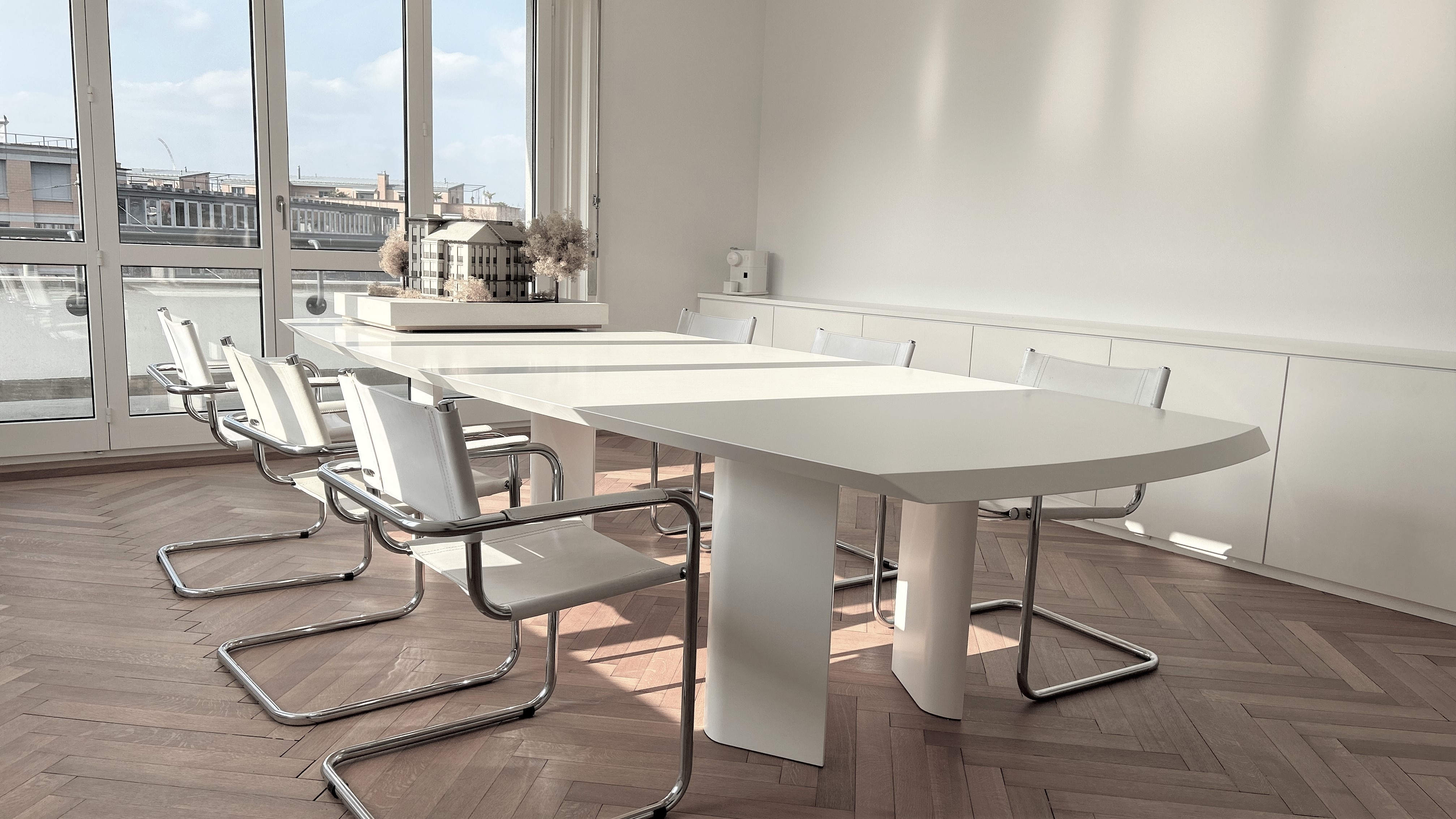 Sitzungszimmer von Lüscher-Lüscher Architekten mit langem weissem Tisch, Freischwingern und Parkettboden.