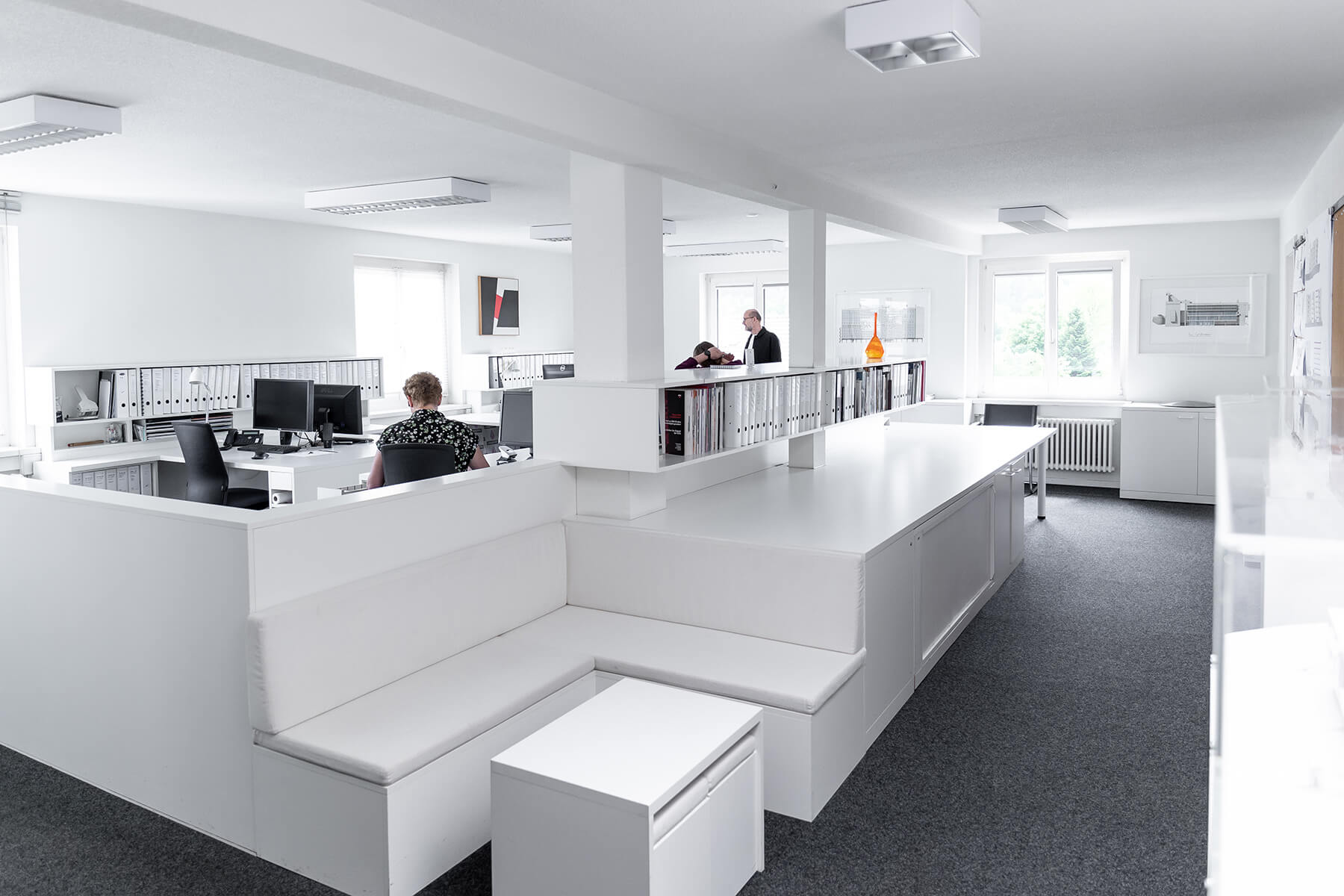 Eingangsbereich von Lüscher-Lüscher Architekten mit weisser Sitzbank und Blick in den offenen Arbeitsraum.