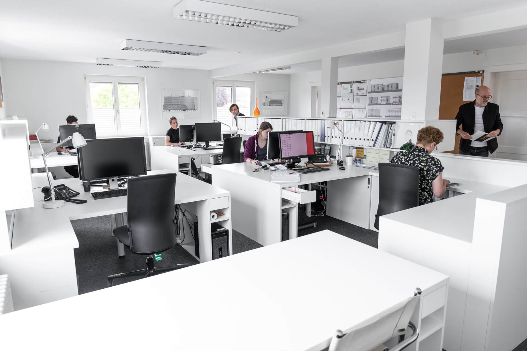 Offener Arbeitsraum von Lüscher-Lüscher Architekten mit weissen Schreibtischen und Mitarbeitenden.