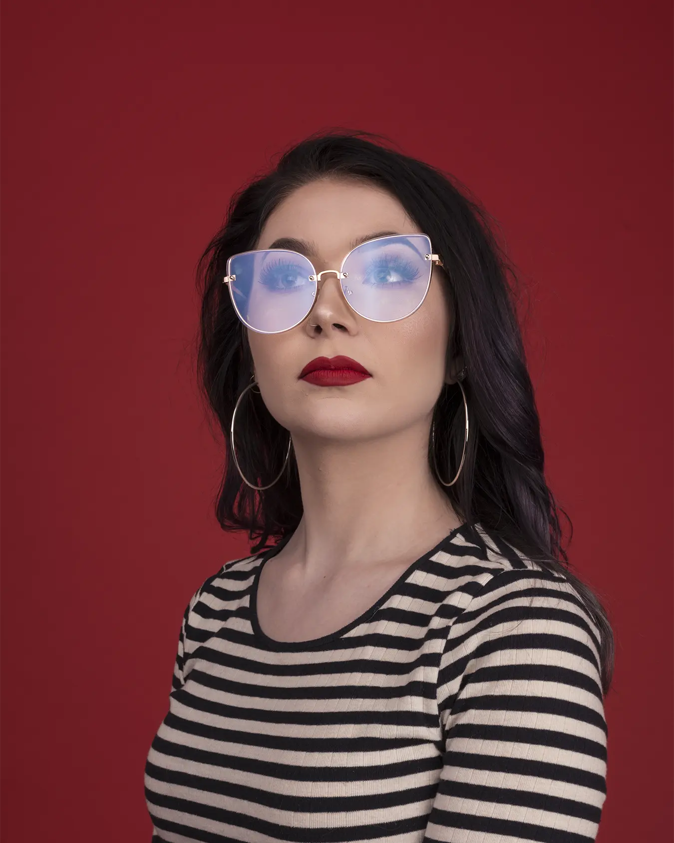Studio photo of Kayln A. on a red backdrop. Her glasses are naturally reflecting the studio lighting.