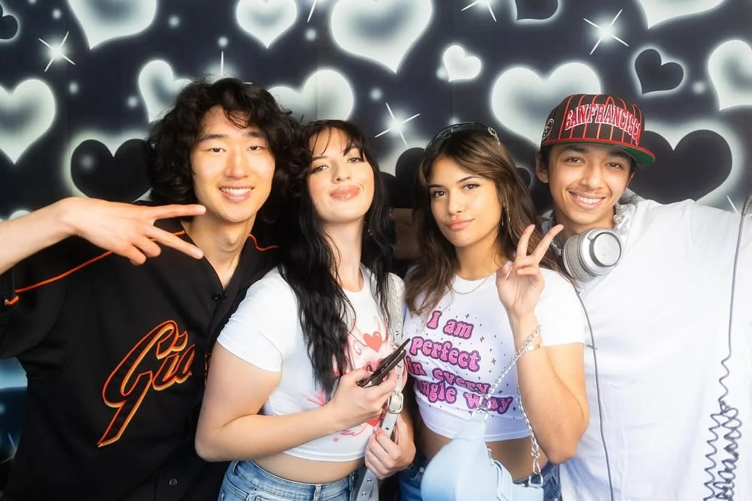 Four performers pose together against a heart-patterned mural.