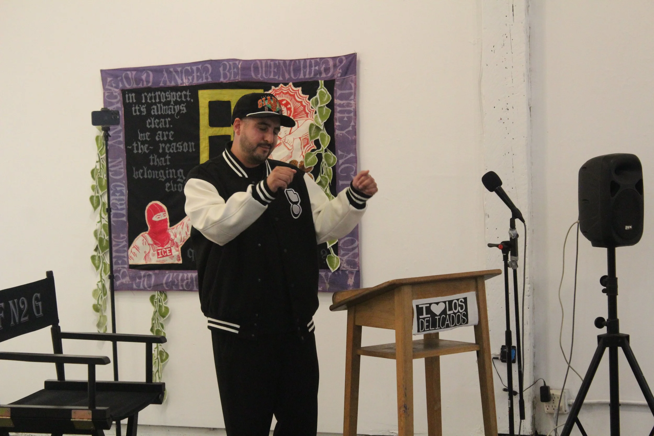 Performer speaking into a microphone beside a gallery lectern.