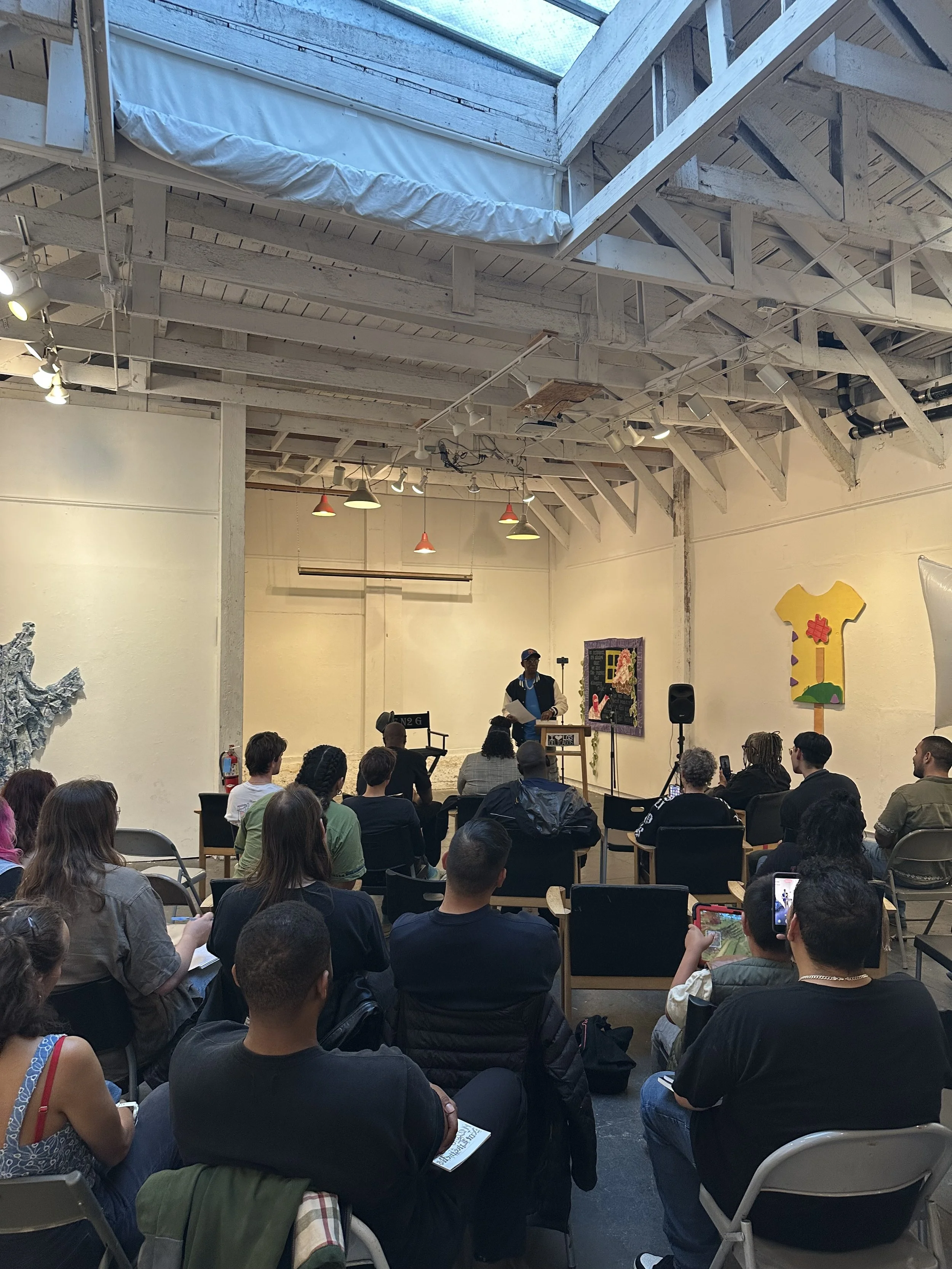 Audience seated beneath skylights at a gallery event.