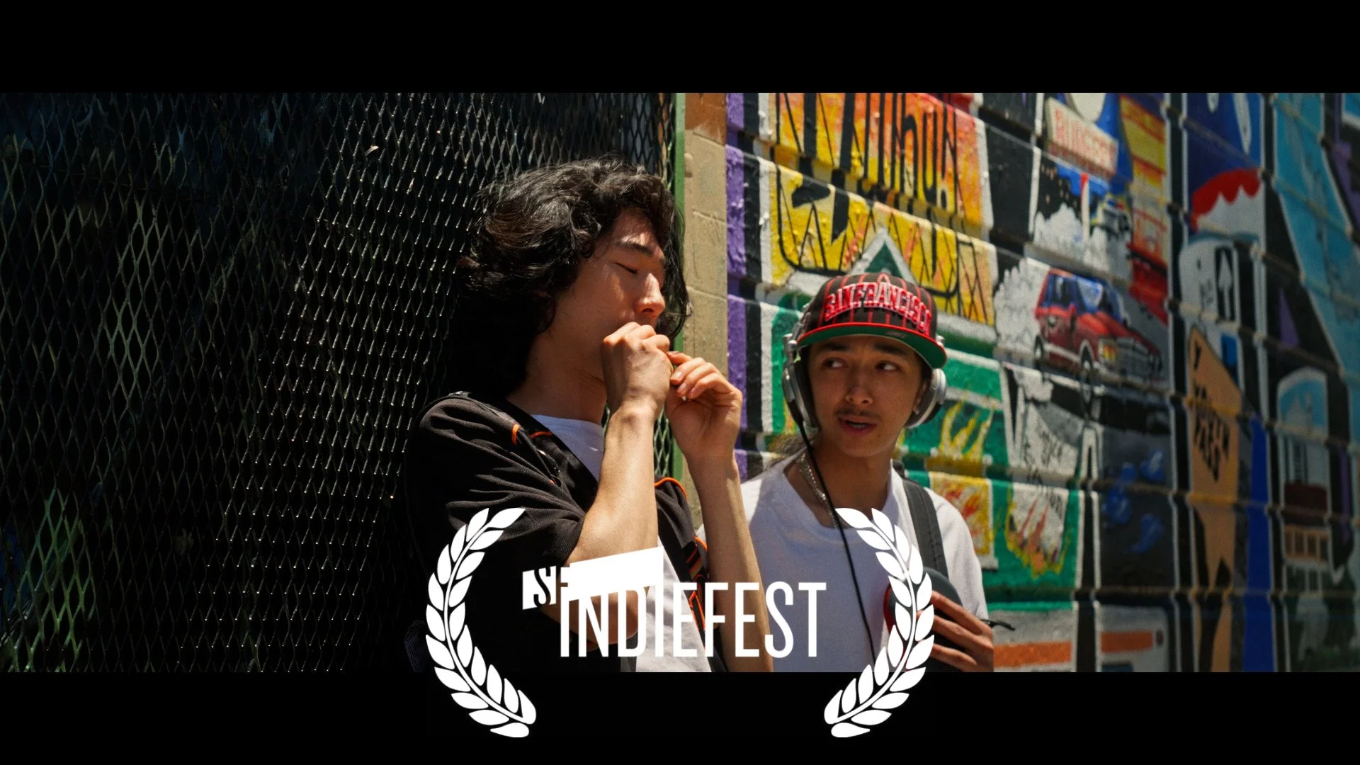 Deville film still beside a colorful mural with an IndieFest laurel.