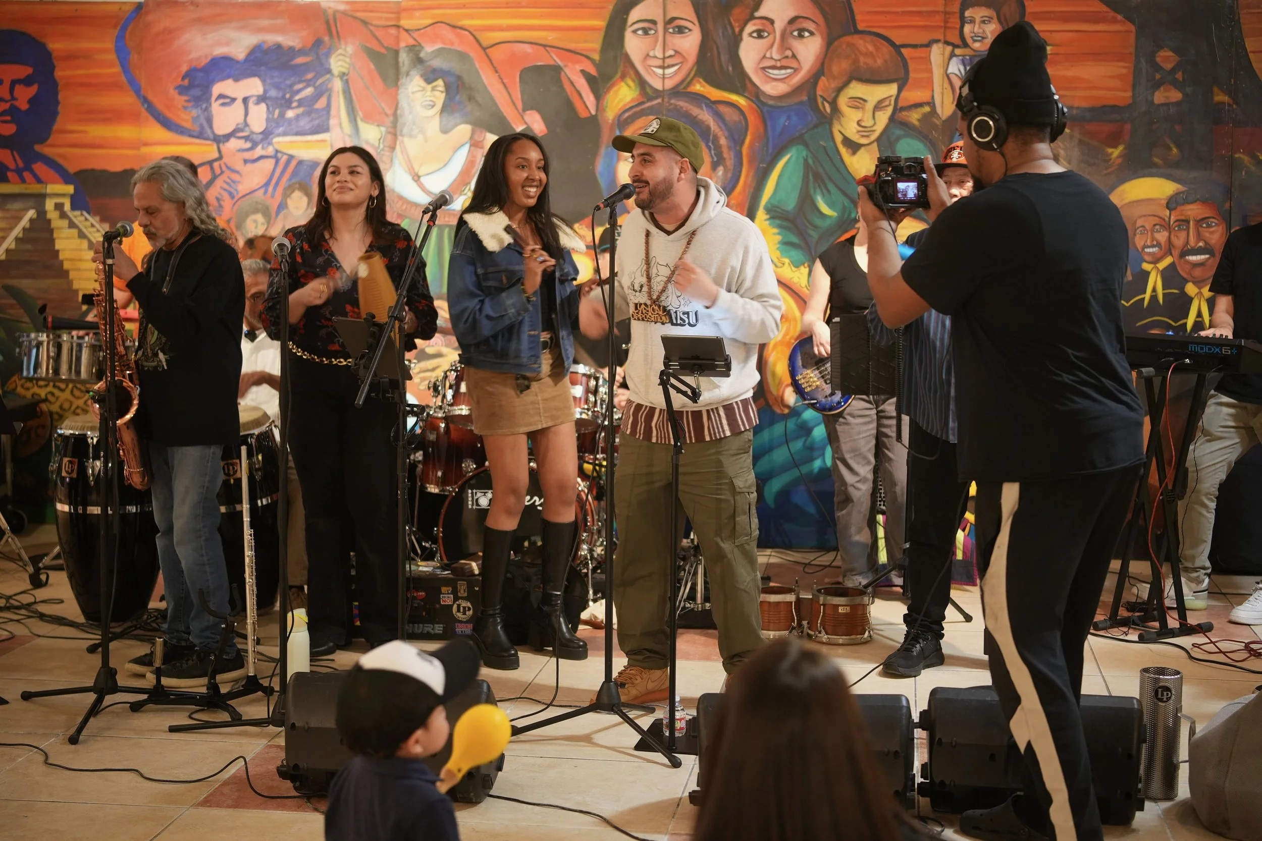 Vocalists and instrumentalists perform in front of a mural.