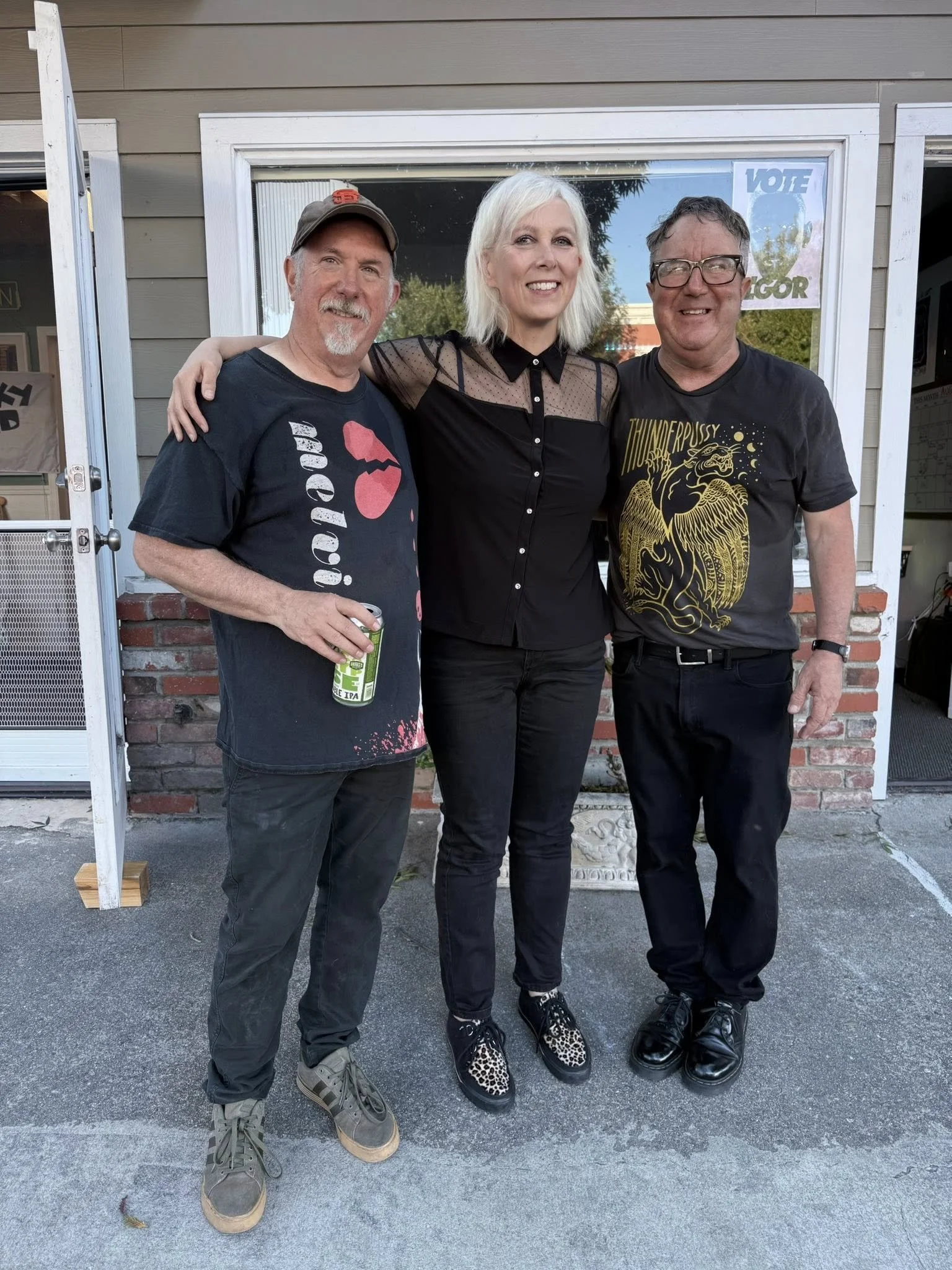 Three band members pose in the storefront doorway.