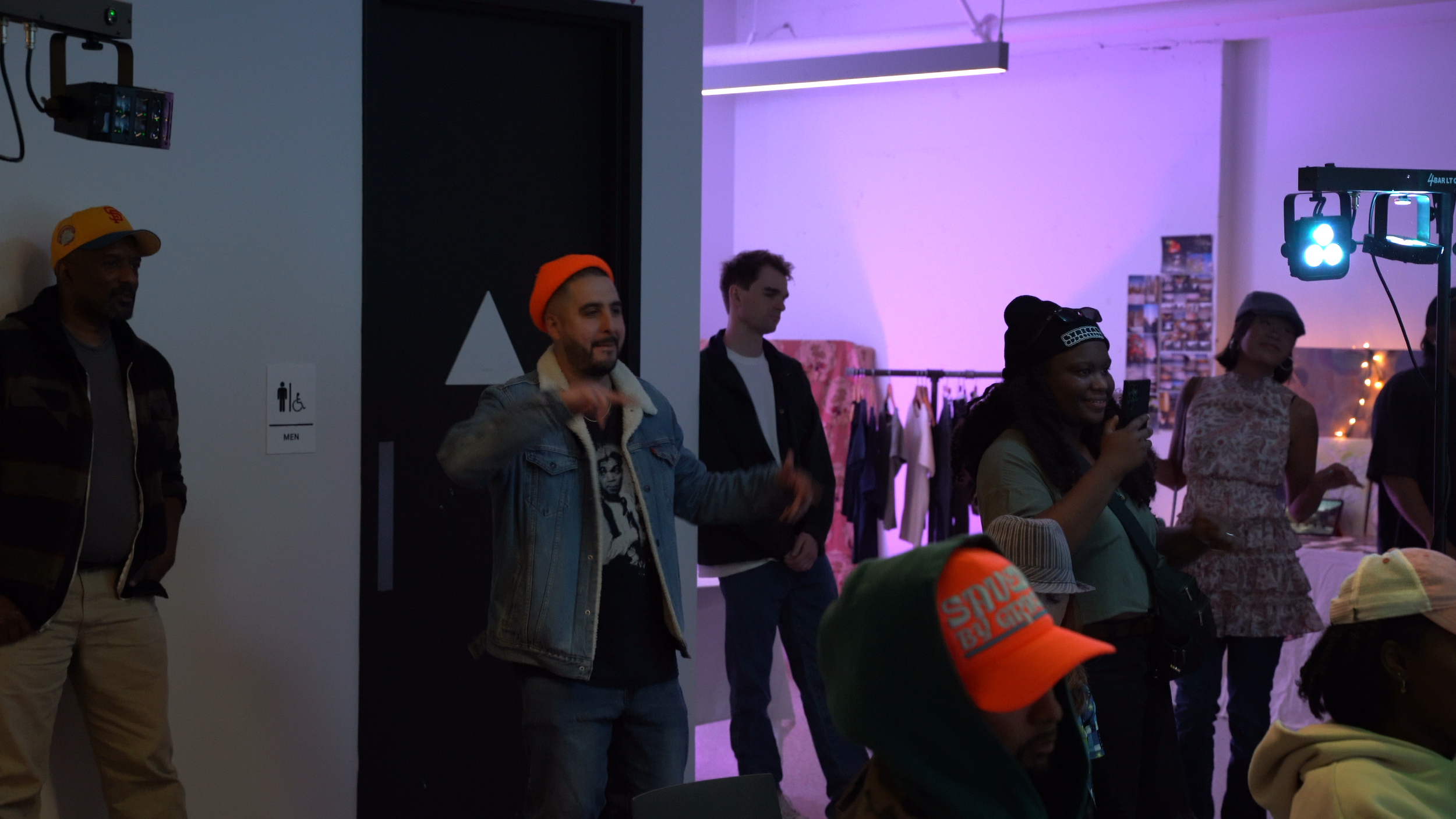 A speaker addresses visitors beside clothing displays.