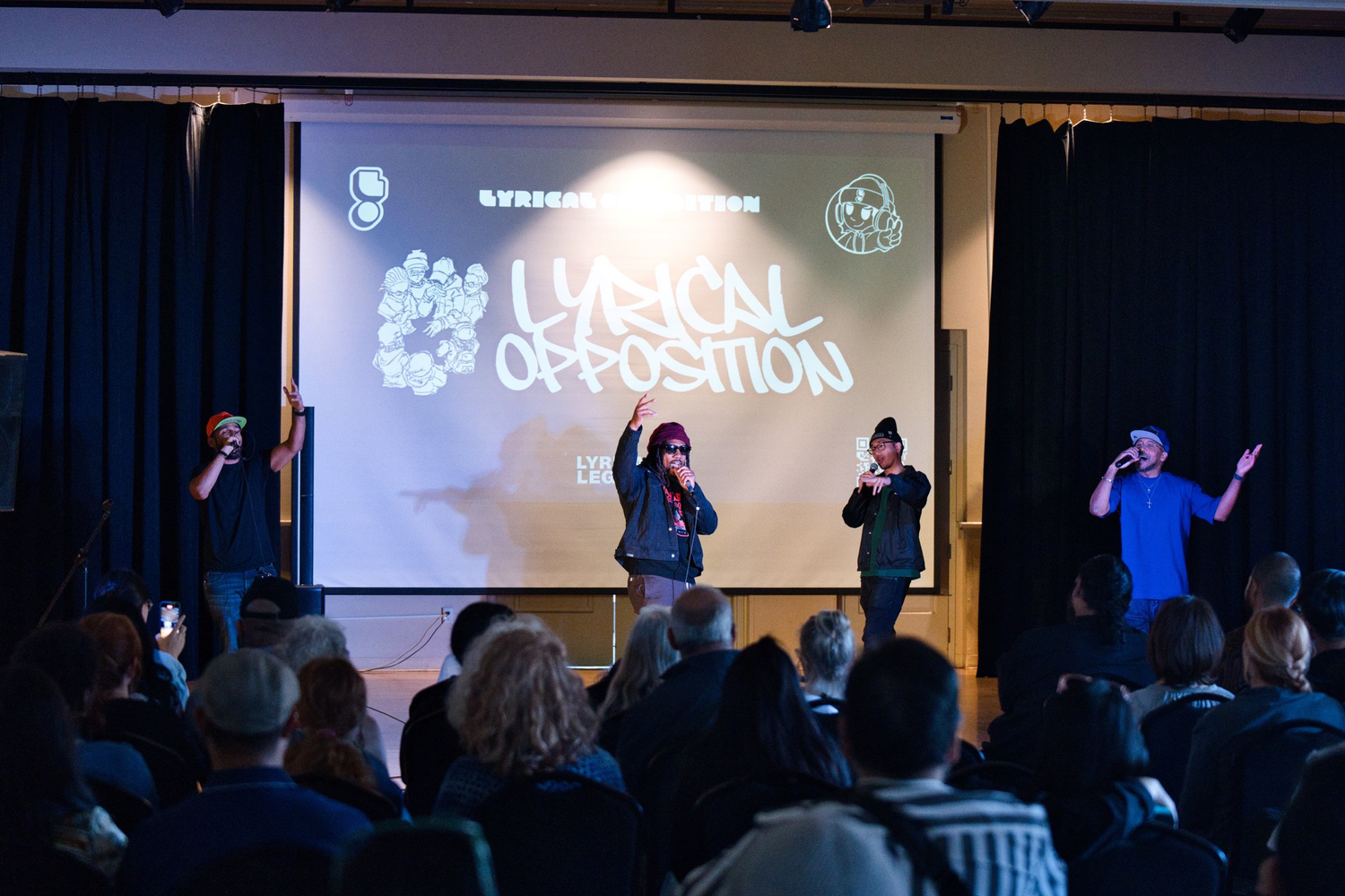 Three vocalists perform in front of a Lyrical Opposition projection.