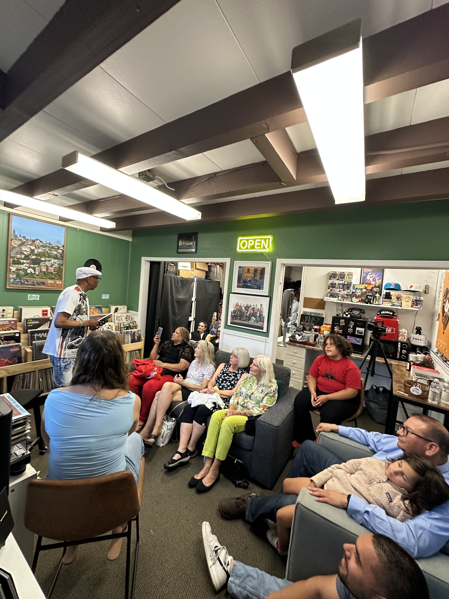Listeners seated around a performer among bookshelves.