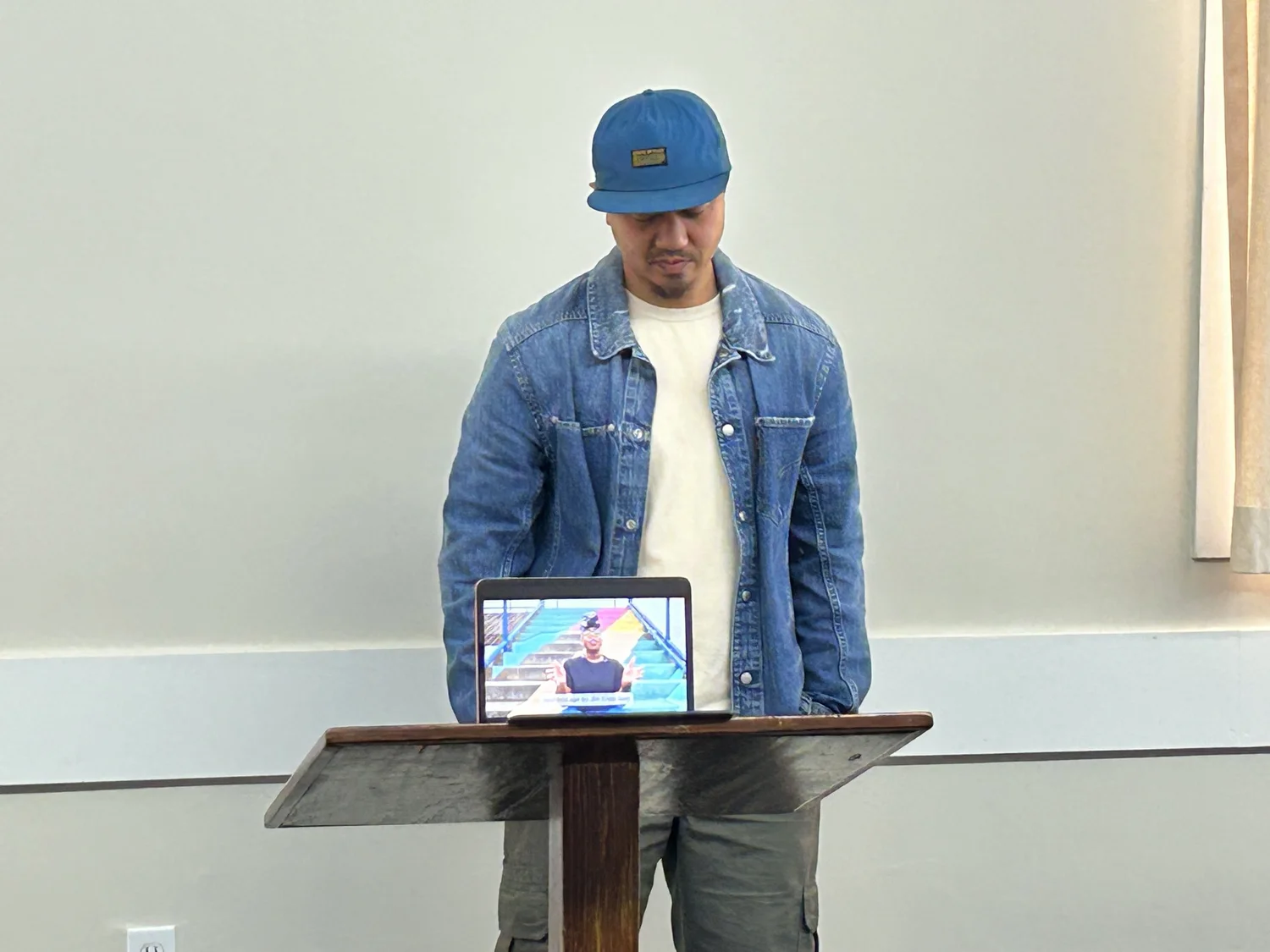 A presenter stands at a lectern with a tablet.