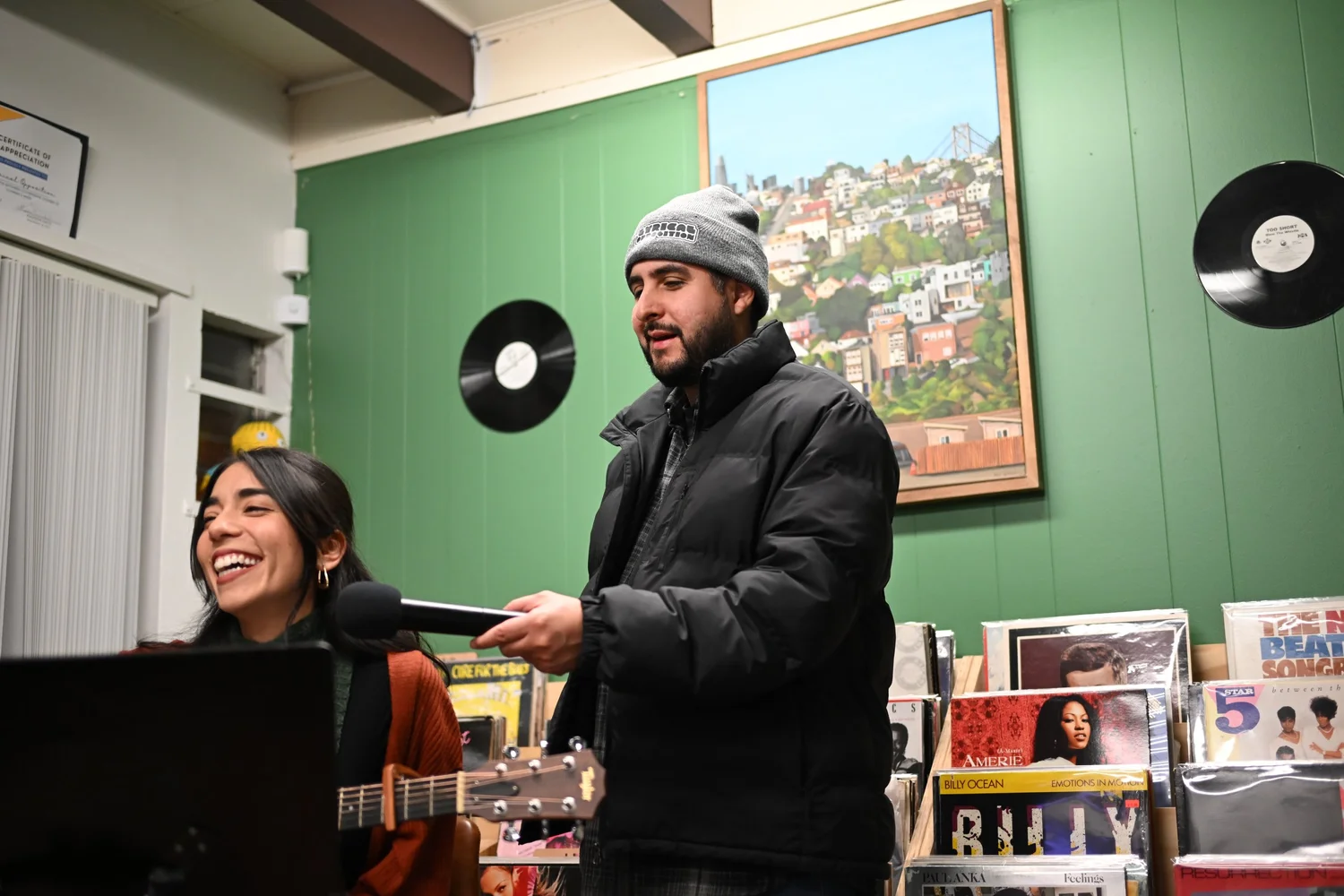 Smiling seated musician with a standing participant holding a microphone.